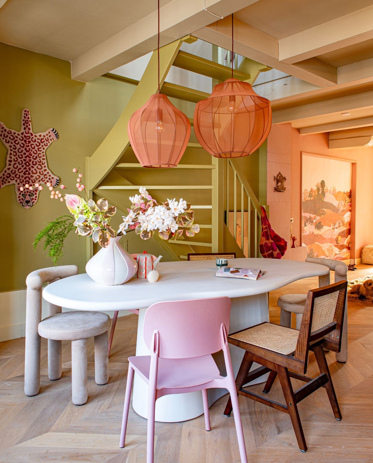 Tafel Giga Meubel. Hanglampen, webbing stoelen en velvet stoelen Westwing. Tijger Doing Goods. Vaas en theepot Karwei. Koffiekop en vloerkleed HKliving. Behang Belarte Studio. Witte poef Fonq. Wandkandelaar van Ibiza. Houten vloer Woodstories. Groenkleur zelf gemengd. Verfkleur beige Cream van Praxis. vtwonen 05-2026 | fotografie Caroline Coehorst