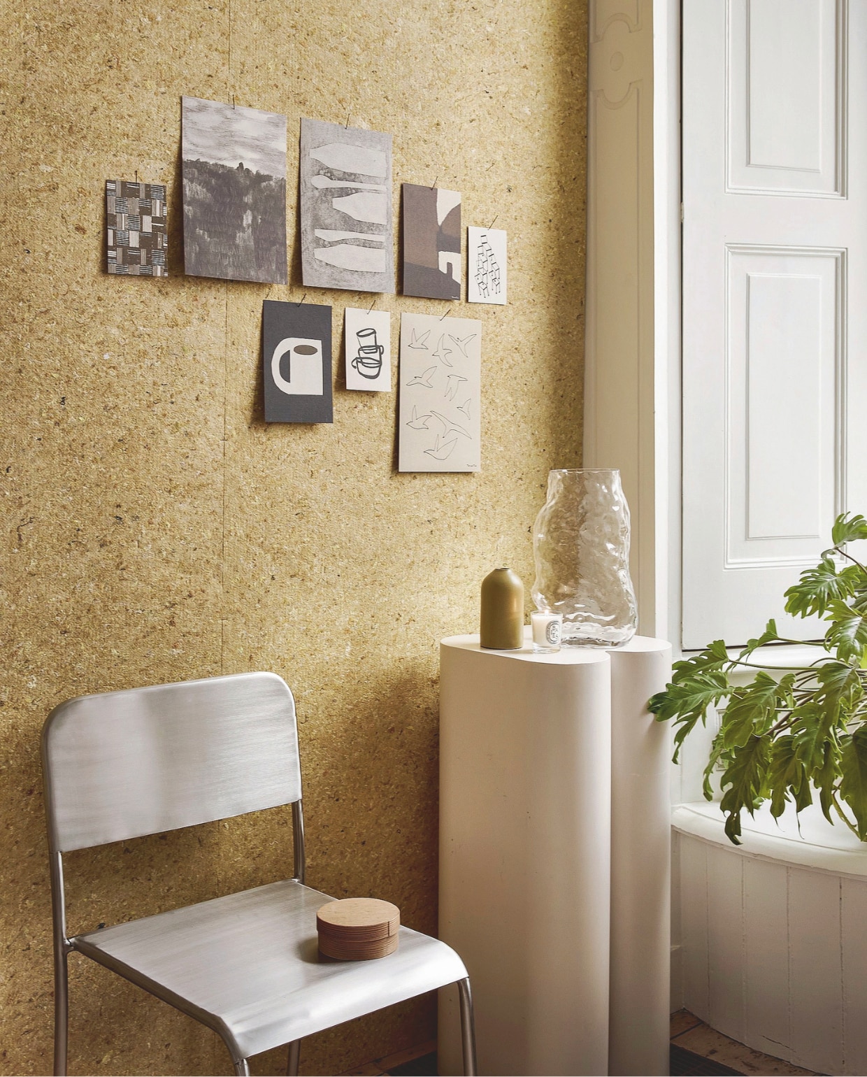 Eijffinger viltbehang Felt Midsummer Yellow, textiel op vliesbehang, 100x90 cm (lxb) € 52,95 (eijffinger.com). Zuiver plantenstandaard Shape, metaal, gebroken wit, 36x35x80 cm en 26x25x60,5 cm (bxdxh), set van 2 € 625,- (shop.vtwonen.nl). Zara Home eetkamerstoel, roestvrij staal, 46x46x80 cm (bxdxh) € 189,- (zarahome.com). Kaarten en prints, per stuk vanaf € 1,95 (estherschuivens.com). Diptyque geurkaars € 40,- (skins.nl). vtwonen 05-2026 | styling Marlies Does | fotografie Peggy Janssen