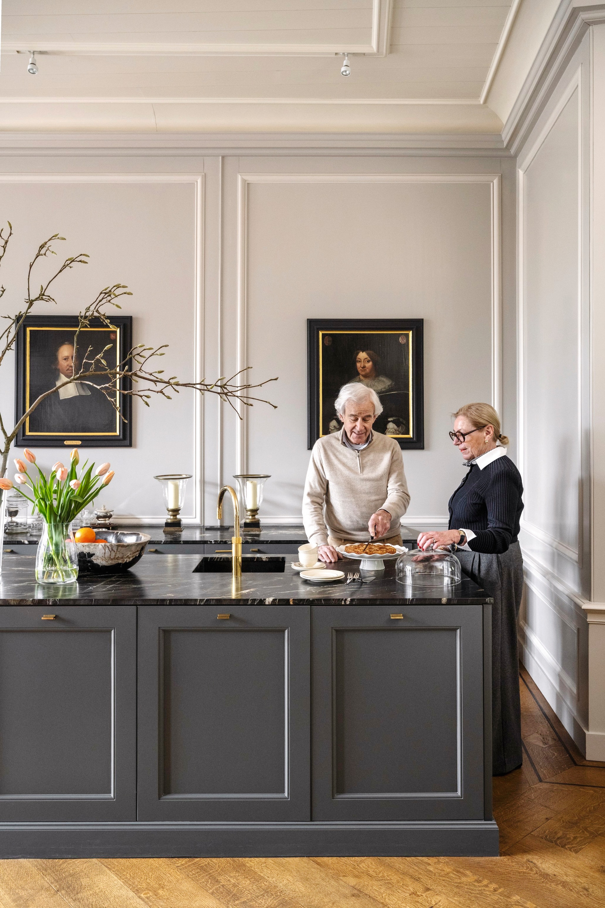 Muurkleur Purbeck Stone, Ammonite en achtergrond boekenkast Mole’s Breath van Farrow & Ball. Keuken, wandbetimmeringen en parketvloer Aannemersbedrijf Leguit en Roos. Kraan Quooker. Vaas Bloemisterij Roos Monnickendam. Schaal Ambiance Laren. Schilderijen en windlichten veiling. Taartplateau cadeau. vtwonen Landelijk 04-2026 | styling Marianne Luning | fotografie Stan Koolen