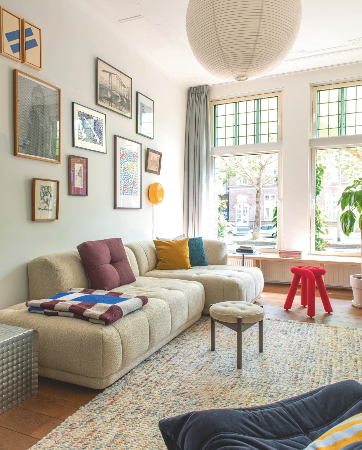 Muurverf Wimborne White en plafondverf Wevet van Farrow & Ball. Gordijnen Kniphal. Bank, hanglamp en sierkussens Hay. Plaid Arket. Rode kruk Moustache. Houten kruk tweedehands. Bijzettafel Tim Teven. vtwonen 05-2026 | fotografie Caroline Coehorst