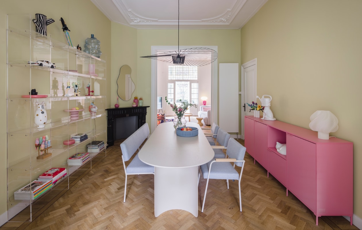 Muurkleur Lemon Tree van Little Greene. Eettafel, bank en stoelen Fést. Dressoir Tylko. Tafellamp Crème Atelier. Lamp Vertigo van Petite Friture. Transparante kast HKliving. Parkieten Pete Cromer voor Prchtg. Spiegel Pond van Ferm Living. Glazen potten Helle Mardahl. Blauwe fruitschaal Ionic van Mae Engelgeer. Slapende kat Vitra. Hond met gieterhoofd Polspotten. Roze taartschaal Form Keramiek.
 vtwonen 05-2026 | styling stylestek | fotografie Eva bloem