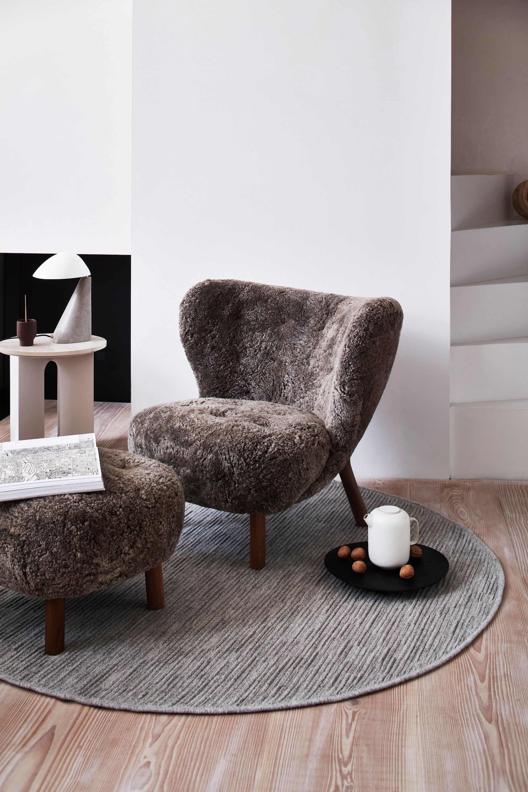 vtwonen vloerkleed Nature cord, wol, antraciet melé, 160 cm (Ø) € 329,-.  M.m.v. vantil.nl (fauteuil, voetenbank), designtales.nl (bijzettafel, tafellamp). Overig privébezit. vtwonen 8-2026 | fotografie Sjoerd Eickmans | styling Danielle Verheul
