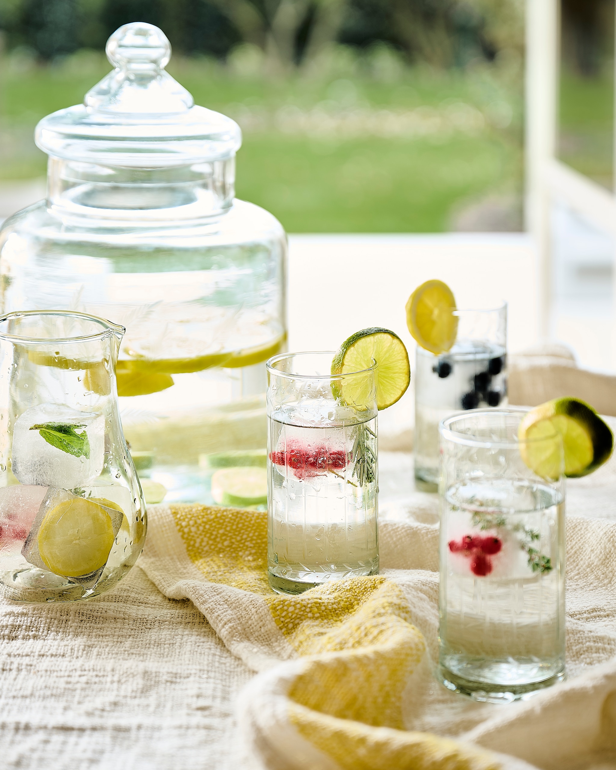 Loberon longdrinkglazen, glas, transparant, set van 6 € 54,95, drankdispenser Cirellis, glas, transparant € 54,95, (loberon.nl). J-line karaf, glas, transparant € 32,-, plaid, katoen, wit en geel, set van 2 € 147,50, (shop.vtwonen.nl). vtwonen Landelijk 07-2026 | Styling Marianne Luning | Fotografie Sjoerd Eickmans