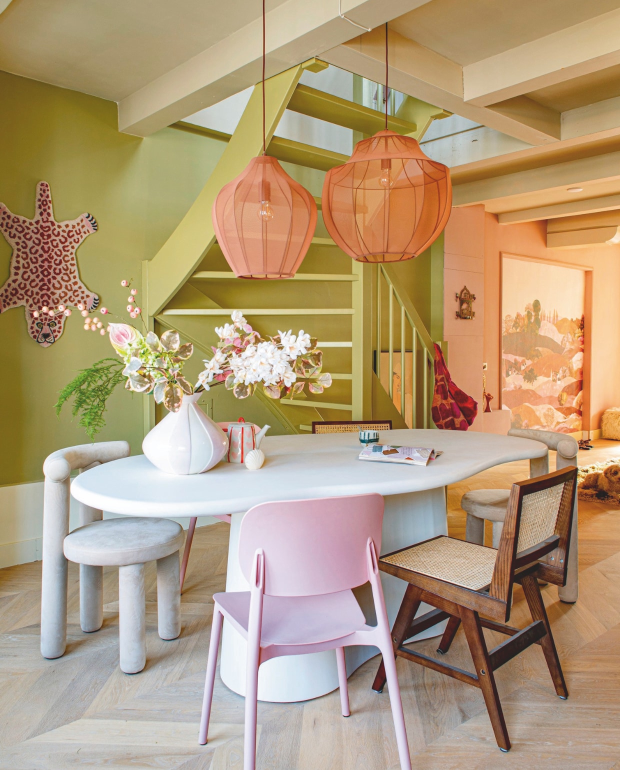 Tafel Giga Meubel. Hanglampen, webbing stoelen en velvet stoelen Westwing. Tijger Doing Goods. Vaas en theepot Karwei. Koffiekop en vloerkleed HKliving. Behang Belarte Studio. Witte poef Fonq. Wandkandelaar van Ibiza. Houten vloer Woodstories. Groenkleur zelf gemengd. Verfkleur beige Cream van Praxis. vtwonen 05-2026 | fotografie Caroline Coehorst
