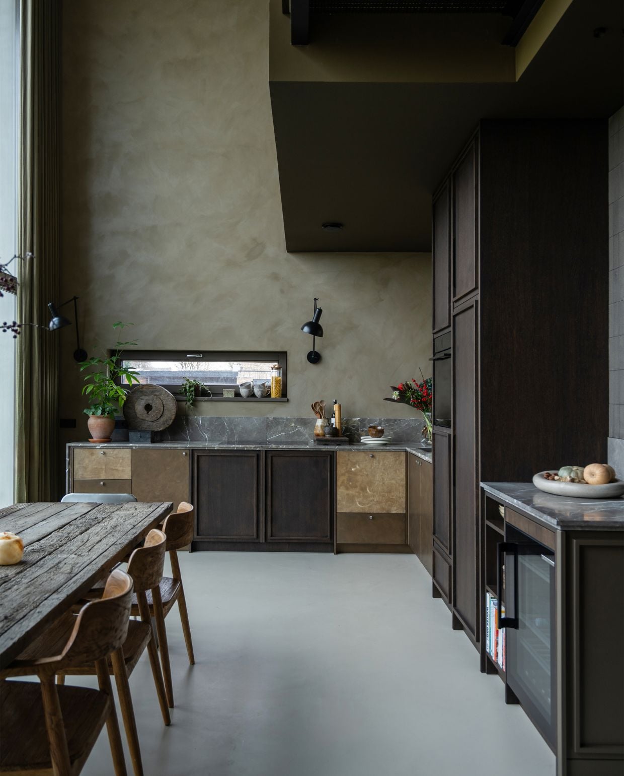 Keuken ontworpen door Jet, gebouwd door Frame Interieurbouw, met aanrechtblad Grillo Natuursteen, en door Roel afgewerkt met metaalstuc en leer. Wand geverfd met kalkverf Mud Soldier van Lab colour the world en afgewerkt met een transparante sealer. Wandlamp Freya van Nordal. Soortgelijk: stoelen Cavel Design, wijnkoelkast Stoves. vtwonen 05-2026 | styling Jet Hendriks | fotografie Lotte van Uittert