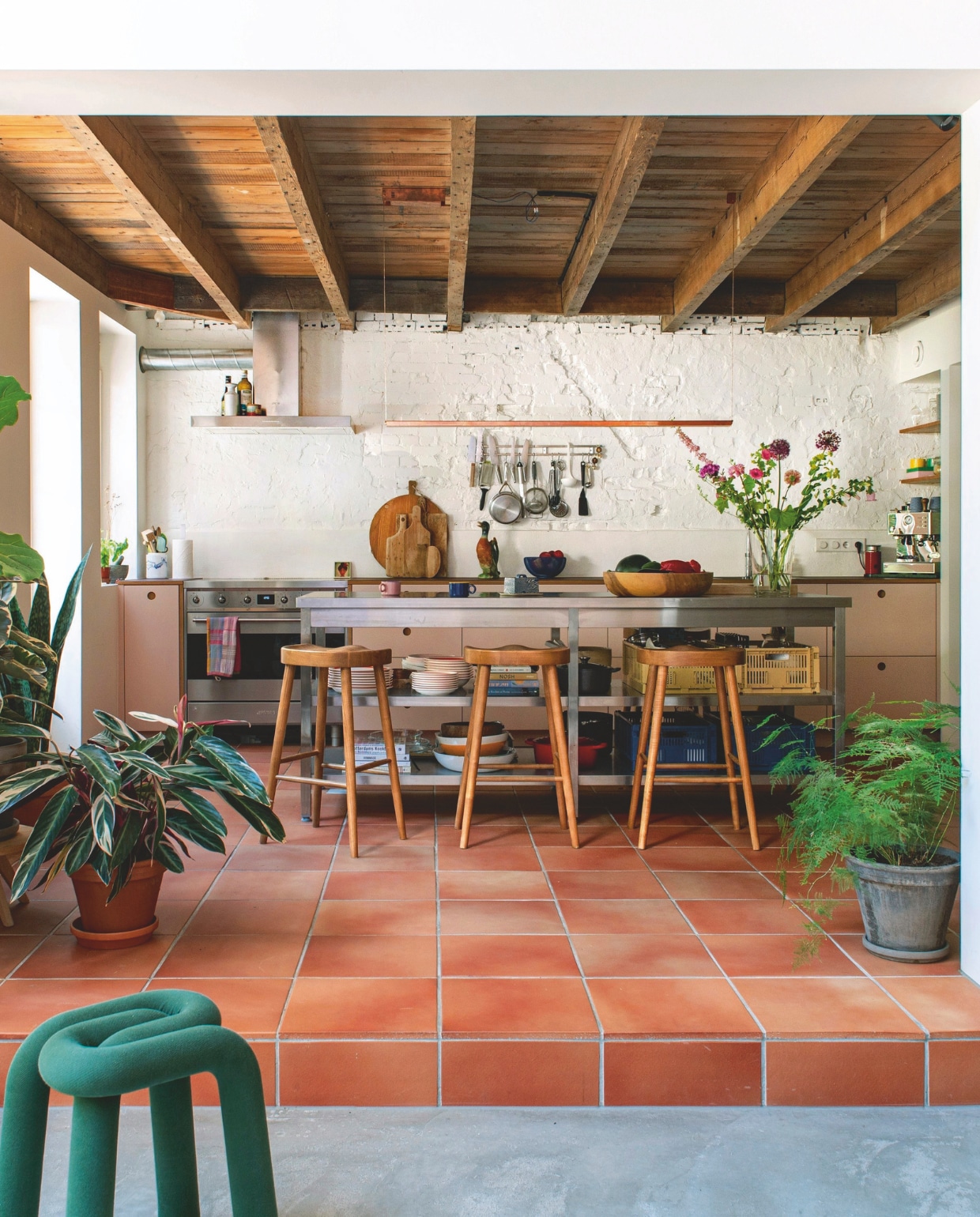 Muurverf Wimborne White van Farrow & Ball. Terracottavloer David en Goliath Antwerpen. Keuken Basis van Reform. Stalen werkbank zelf ontworpen. Barkrukken Zara. Hanglamp Piet Hein Eek. Houten schaal Kinta. Waterkan van St. Clément vintage. Kratten Hay. Keukengereihouder Veark. Groene kruk Moustache. vtwonen 05-2026 | fotografie Caroline Coehorst