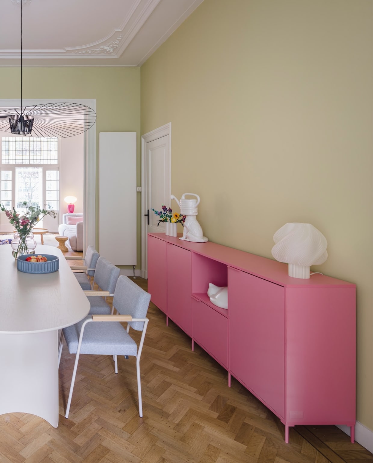 Muurkleur Lemon Tree van Little Greene. Eettafel, bank en stoelen Fést. Dressoir Tylko. Tafellamp Crème Atelier. Lamp Vertigo van Petite Friture. Transparante kast HKliving. Parkieten Pete Cromer voor Prchtg. Spiegel Pond van Ferm Living. Glazen potten Helle Mardahl. Blauwe fruitschaal Ionic van Mae Engelgeer. Slapende kat Vitra. Hond met gieterhoofd Polspotten. Roze taartschaal Form Keramiek.