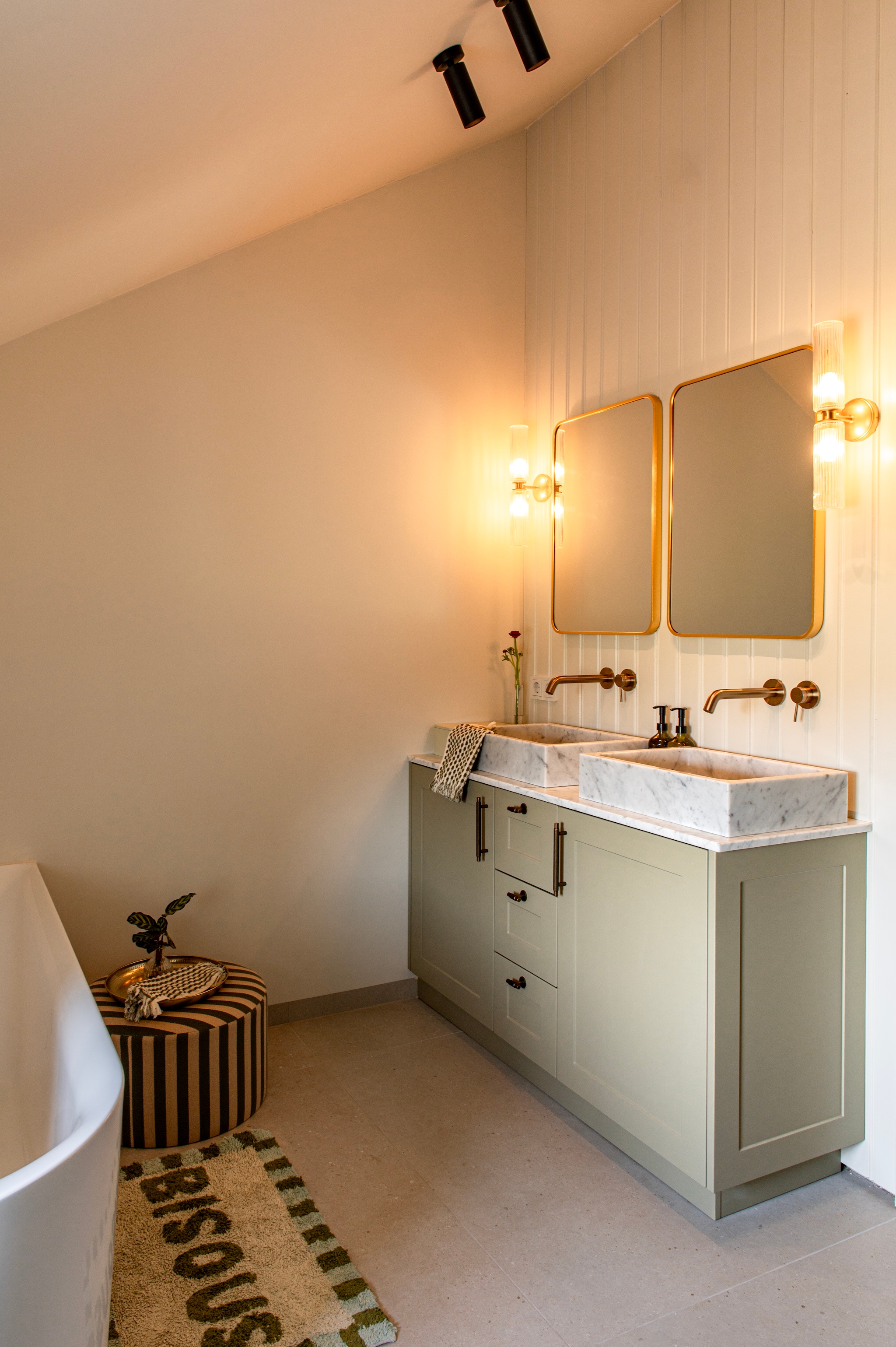 Wastafelmeubel met marmeren waskommen en messing kranen maatwerk van Eik-punt. Kast in Jade van Lab Paint. Wandlampen Corston. Spiegels Fonq. Badmat Westwing. Poef Søstrene Grene. Muurkleur School House White van Farrow & Ball. vtwonen Special 03-2026 | fotografie Caroline Coehorst | productie De Binnenkijkers by Caroline