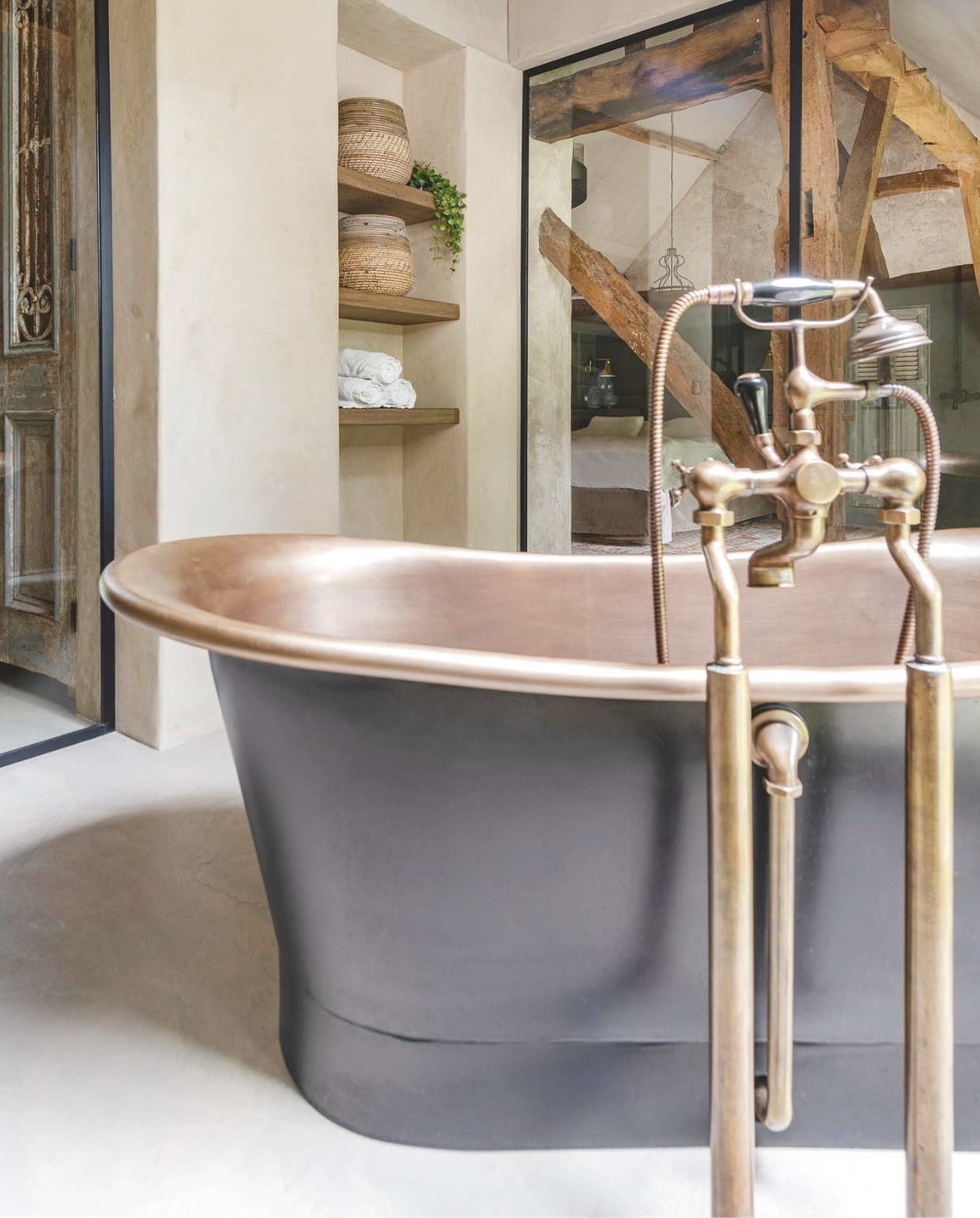 Vrijstaand Duke Bad van Kenny & Mason via Taps & Baths met zwarte buitenkant en authentieke messing binnenkant, afgeschermd door een smeedijzeren wand. vtwonen Landelijk 05-2026 | productie Tabs & Baths | fotografie Claude Smekens