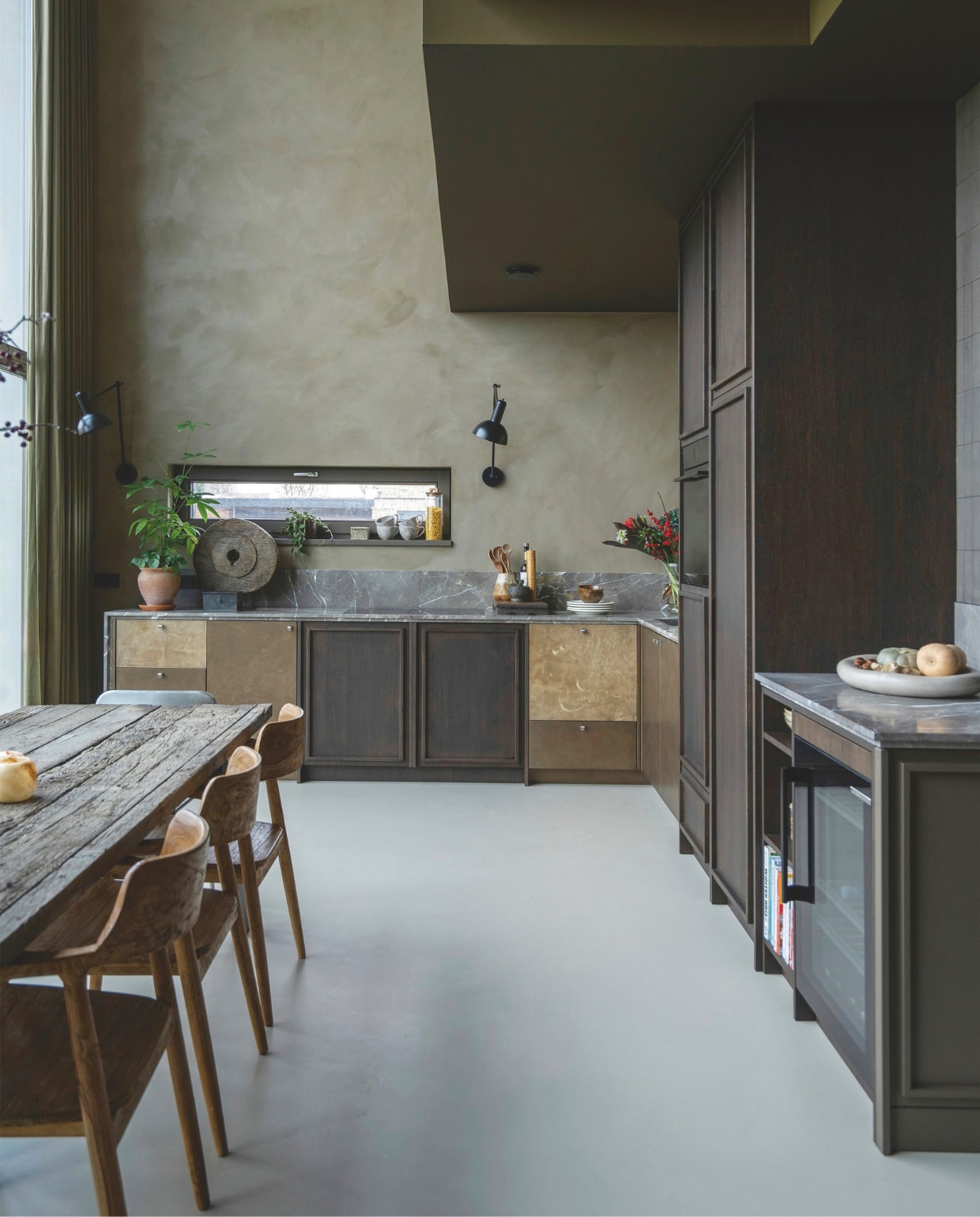 Keuken ontworpen door Jet, gebouwd door Frame Interieurbouw, met aanrechtblad Grillo Natuursteen, en door Roel afgewerkt met metaalstuc en leer. Wand geverfd met kalkverf Mud Soldier van Lab colour the world en afgewerkt met een transparante sealer. Wandlamp Freya van Nordal. Soortgelijk: stoelen Cavel Design, wijnkoelkast Stoves.  vtwonen 05-2026 | styling Jet Hendriks | fotografie Lotte van Uittert