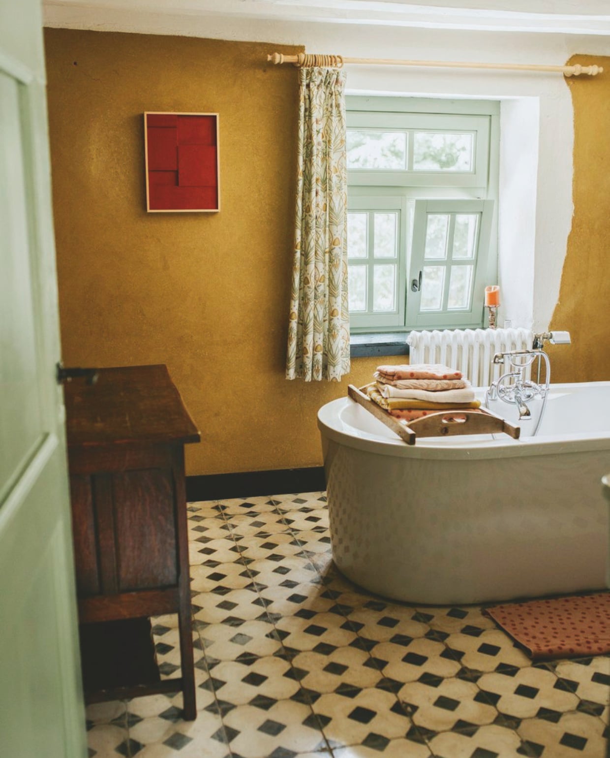 Muurkleur leemstuc. Kozijnkleur Breakfast Room Green van Farrow & Ball. Gordijnen The Chateau. Kast uit familie. Schilderij Th Studio Nootdorp. Vloertegels oude bouwmaterialen kasteelvloer. Dienblad Kringloop.  Kleed Hema. Handdoeken Hema, Sissy-Boy en Anthropologie. vtwonen zomerspecial 2026 | styling Puck Hommerter, Eva Krebbers | fotografie Eva Krebbers (Tumbleweed & Fireflies Photography)