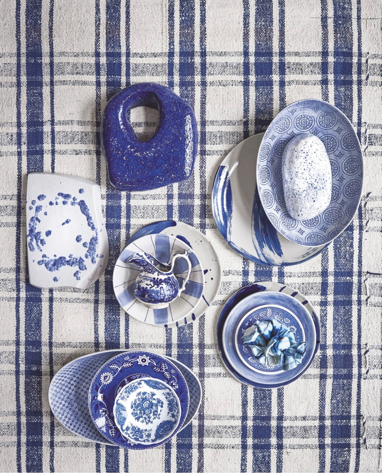 Blauw geruit vintage kleed, prijs op aanvraag, ovale schalen Etosha mixed pattern € 46,-, Heartwear kaars in stof,  fairtrade, indigo € 79,- (mvninteriors.com). Atelier de Rijk kunstwerken, keramiek, prijs op aanvraag (atelierderijk.com). Tableware Amsterdam Maastricht blauw keramiek, vanaf 18,- (tableware.amsterdam). Serax borden Sophia, met kalligrafievegen, ontwerp van Marie Michielssen, blauw en beige, 22 cm (Ø), set van 4 € 116,- (serax.com). Overig privébezit. vtwonen Landelijk 05-2026 | styling Kelly van Gendt en Liza Wassenaar | fotografie Alexander van Berge
