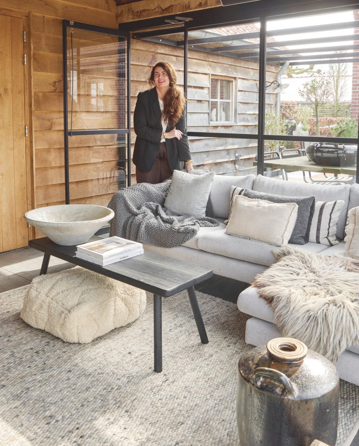 Bank Ikea. Keramische tegelvloer. Vloerkleed De Agave Natuurlijk Wonen. Stalen pui Metalura. Sprei H&m. Texelse Schapenvacht. Salontafel, boeken en vierkante kussen De Tuynkamer. Kussens Katoo Fashion&living. Poef Studio Pure. Schaal Snufenshoe. vtwonen Landelijk 05-2026 | styling Kristel van Leeuwen | fotografie Peggy Janssen