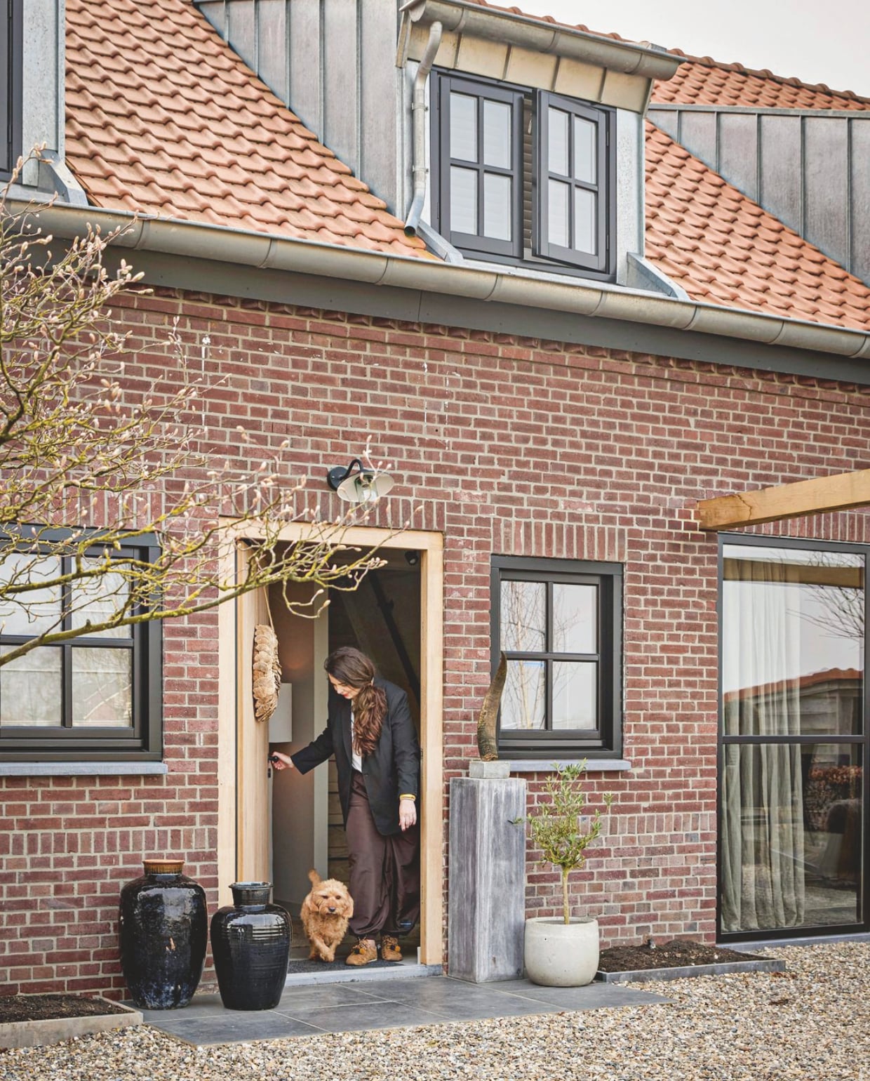 Jennifer met hond Pien. Verfkleur kozijn Ral 9005. Boom en pot Intratuin. Vazen antiekmarkt België. Op de grond liggen keramische tegels en gemengd grind.