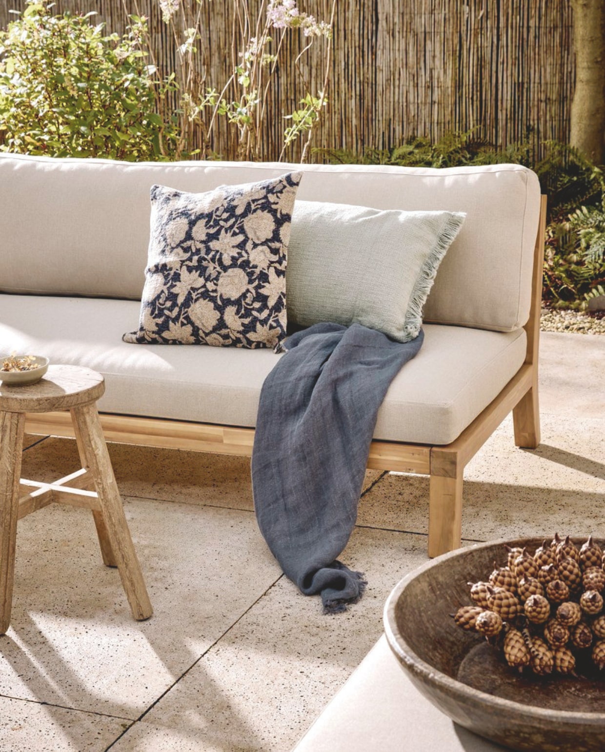 vtwonen hocker/bijzettafel Relax, fsc-gecertificeerd acaciahout en polyester kussen in naturel/zand, 90x60x40 cm (bxdxh) € 349,-. tuinbank Relax, fsc-gecertificeerd acaciahout en polyester kussens in naturel/zand, 180x90x70 cm (bxdxh) € 749,-, vtwonen loungestoel Relax, fsc-gecertificeerd acaciahout en polyster kussens, naturel en zand, 120x70x90 (bxdxh) € 549,-. M.m.v. zarahome.com (kussens, vaas), hetkabinet.nl (mand, vloerkleed, grote houten schaal). Overig privébezit. vtwonen collectie 5-2026 | styling Kim van Rossenberg | fotografie Sjoerd Eickmans