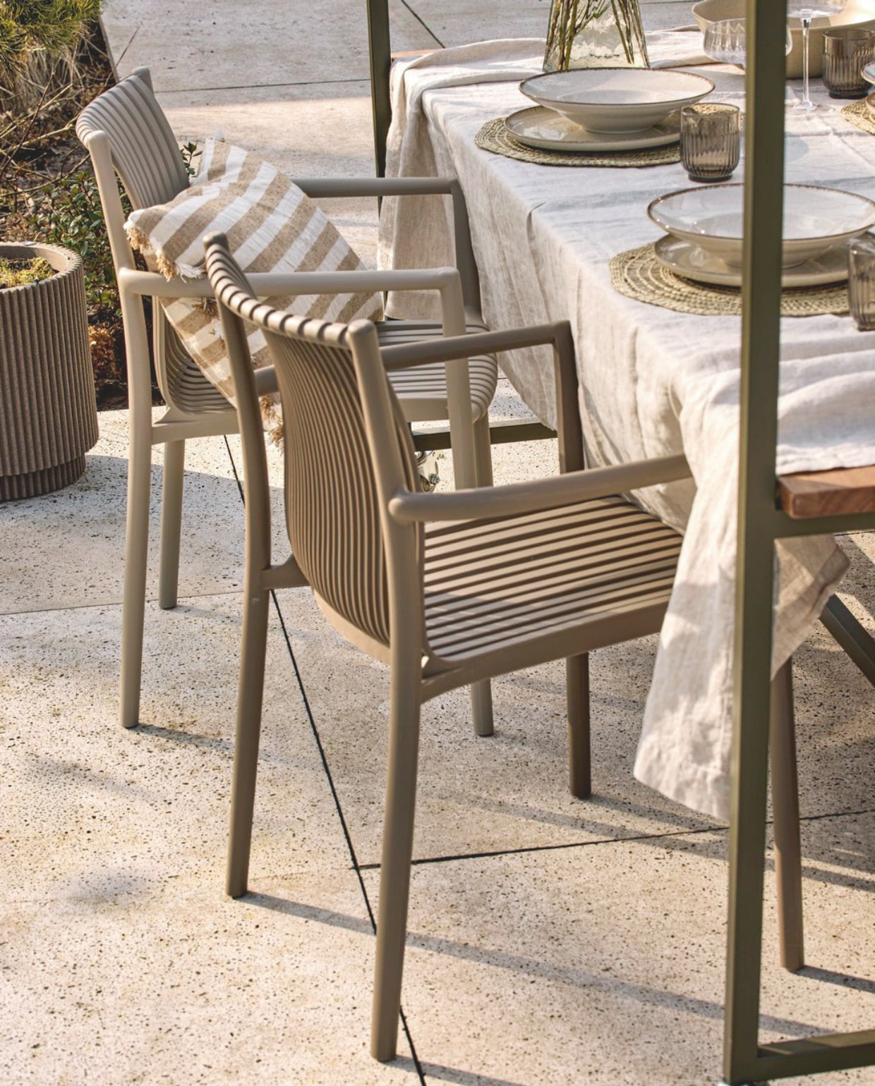 vtwonen tuinstoel Easy Going, kunststof, zand en bruin, 56x57x84 cm (bxdxh) € 99,95.  M.m.v. zarahome.com (kussen, beige servies), loods5.nl (glazen kan, glazen). Overig privébezit. vtwonen collectie 5-2026 | styling Kim van Rossenberg | fotografie Sjoerd Eickmans
