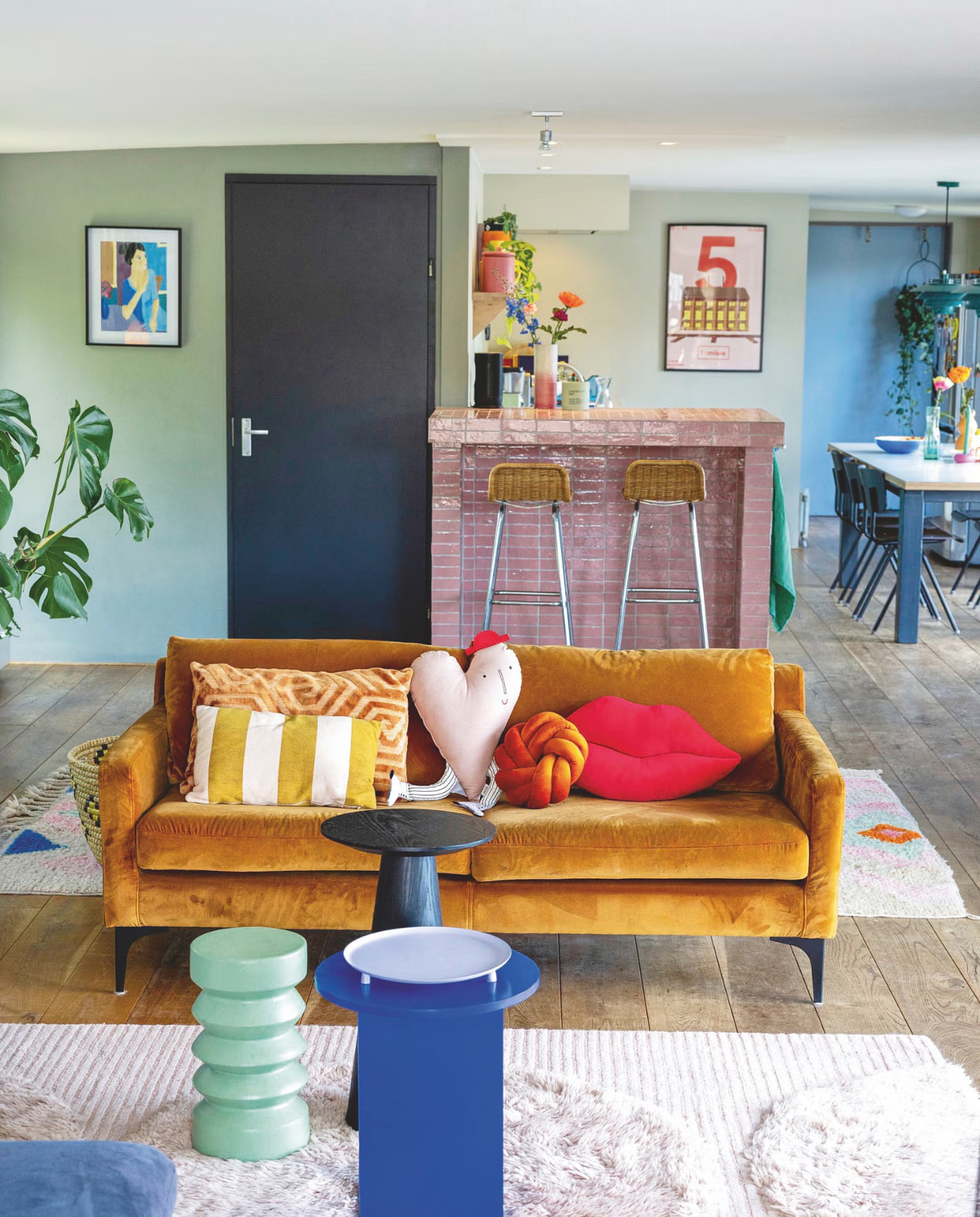 Wandkleur Pigeon en kleur deur Off Black van Farrow & Ball. Bank Sofa Company. Groene bijzettafel HKliving. Zwarte en blauwe bijzettafel, paarse schaal, knoop-kussen, lipkussen, bruin velours kussen en mand Kwantum. Gestreept kussen Hema, hartkussen Ferm living. Roze tapijt Jotex, gekleurd tapijt Etsy. Vintage barkrukken van Rohé Noordwolde via Reliving. Tegels bar Designtegels. Roze vaas en schilderijmet blauwe dame kringloopwinkel. Roze voorraadpot Kitsch Kitchen. Handdoek Hema. Poster van filmtheater Lumière Maastricht. Eettafel zelfgemaakt, stoelen eromheen Revolt via Machinekamer. Blauwe schaal op keukentafel Rice. vtwonen 05-2025 | styling Ilona Jongepier | fotografie Dana van Leeuwen