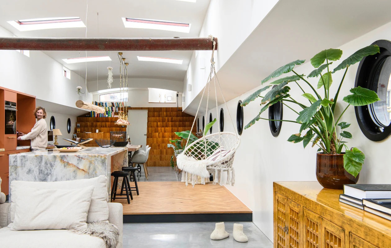 Podium van eikenhout. Hangstoel Casa. Dankzij slim geplaatste ramen in het dak komt er veel daglicht binnen. De ronde patrijspoorten dragen bij aan de nautische sfeer. vtwonen 05-2025 | styling Marit Saladini | fotografie Louis Lemaire