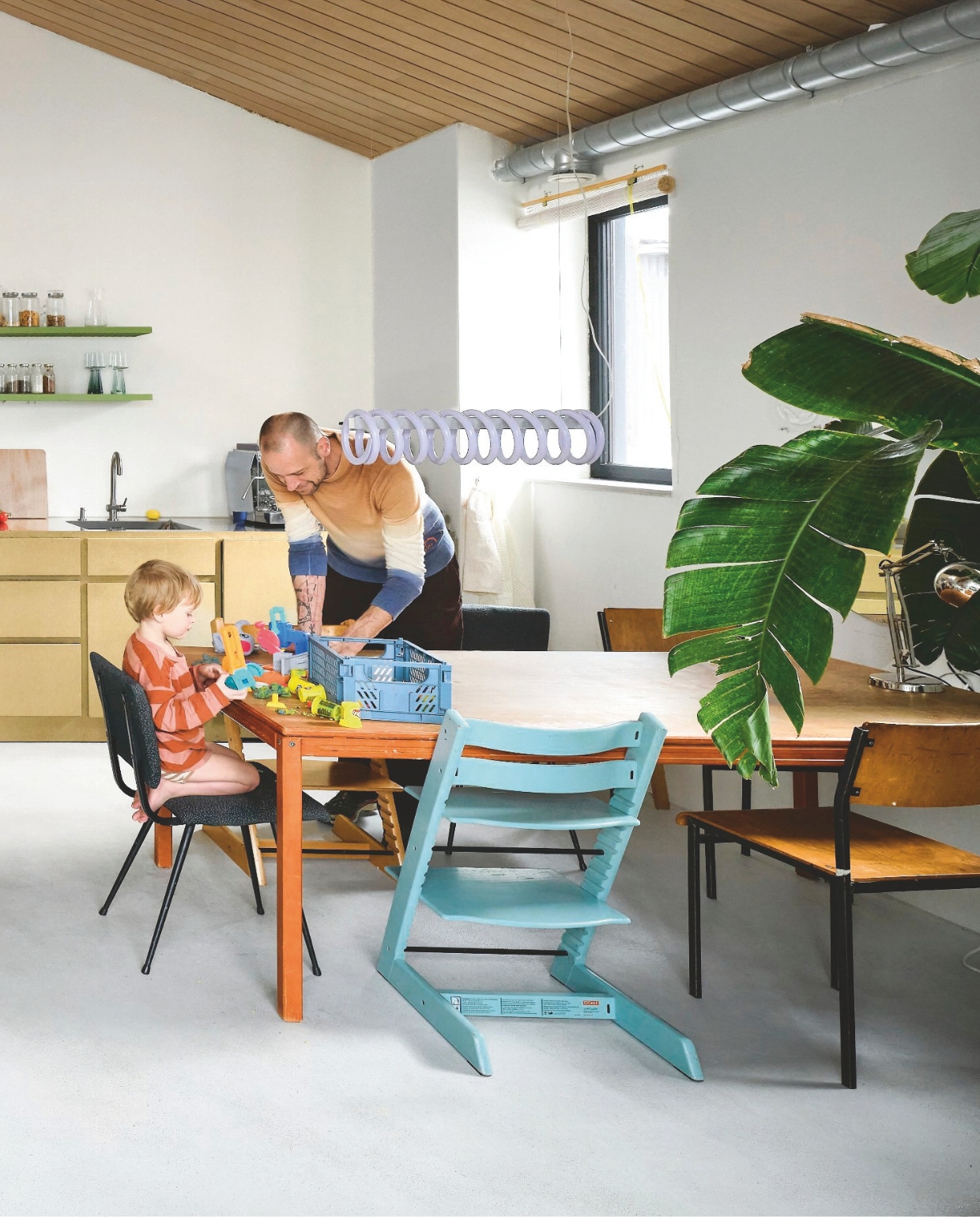 Houten krukken en hanglamp eigen ontwerp van Dirk. Keuken van gecoat vochtwerend mdf met wandplanken van gekleurde rasters van rvs. Op de plank: vaas van Willem van Hooff. Houten tafel is een oud bureau van Alissa. Kunstwerk links cadeau van vrienden. Stoelen Brabantia, opnieuw bekleed. Bank Splitback van Innovation Living. vtwonen 06-2026 | fotografie Mr. Frank