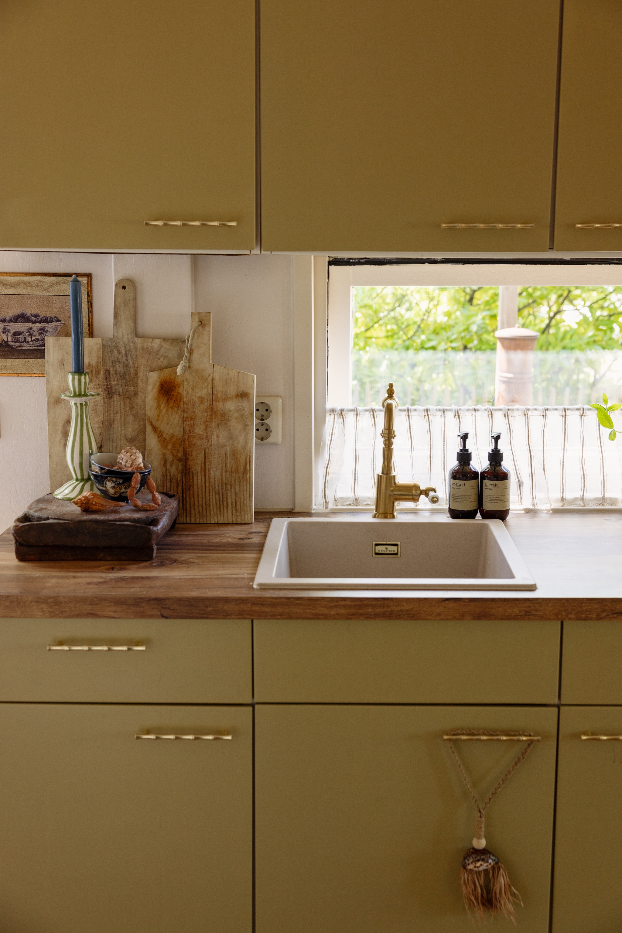Keuken geverfd in Olive oil van Little Greene. Aanrechtblad Karwei. Kraan Ikea. Handgrepen Etsy. Kandelaar Anna + Nina. Houten vintage plateau uit India Van Verre Interior. Zeeppompjes Meraki. Cafégordijntje zelfgemaakt. vtwonen 08-2026 | styling Sophie Dirven | fotografie Dana van Leeuwen