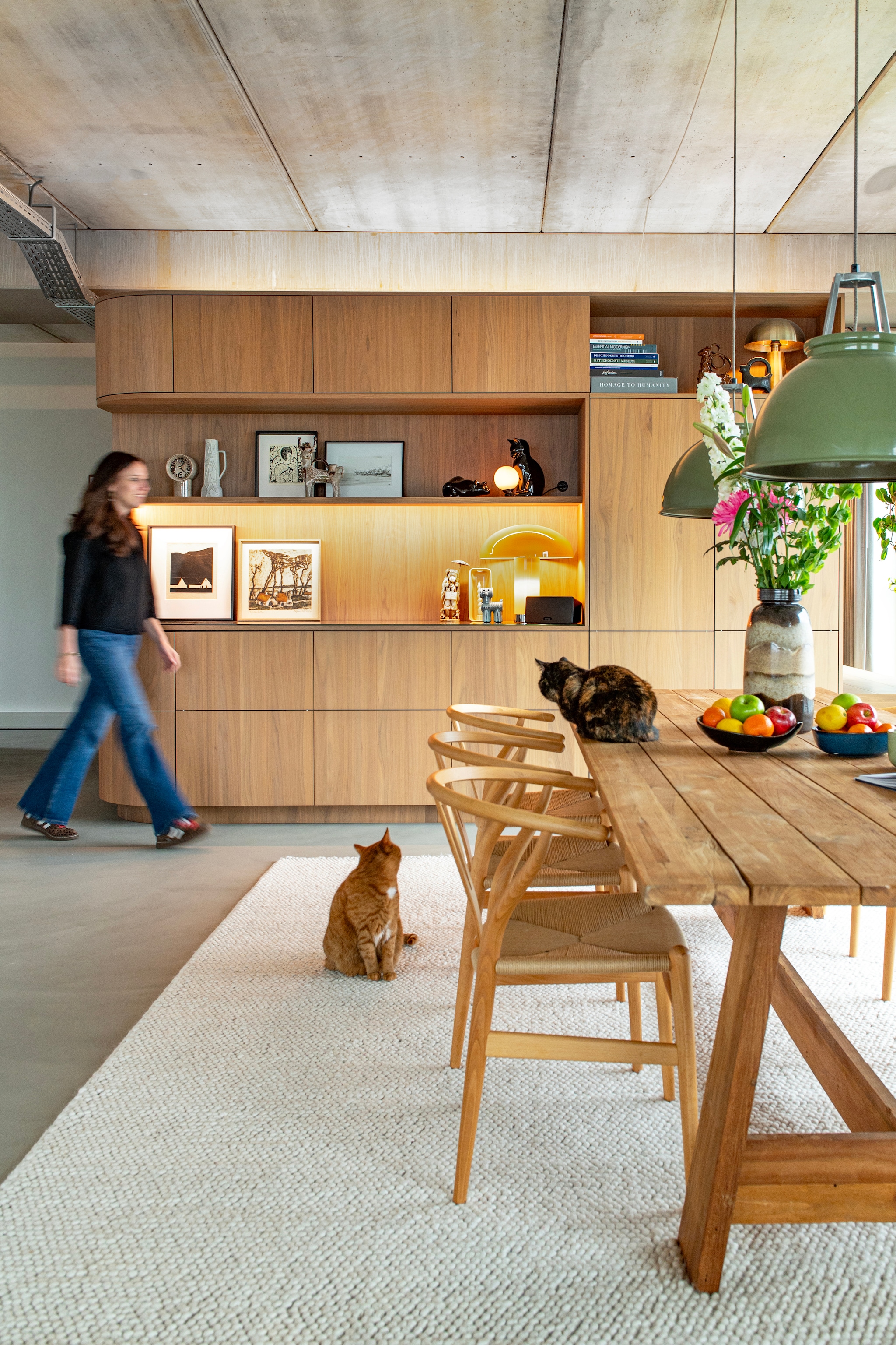 Multifunctioneel meubelblok ontworpen door Vervoort Architecten, uitgevoerd in shinnoki frozen walnut door Vos Interieur. Tafel Loods 5. Stoelen Wishbone van Hans J. Wegner voor Carl Hansen & Søn. Hanglampen Titan van Original Btc. Klok en tafellamp Lounge mocha van HKliving. Vloerkleed Trendcarpet. Lavasteen gietvloer Berkers Vloeren. Vintage kunstwerken: zwart-wit lithografie van Albert Bertelsen, kleurenets van Alfons Blomme, ets Meisje met kat van Britta Nehrman.