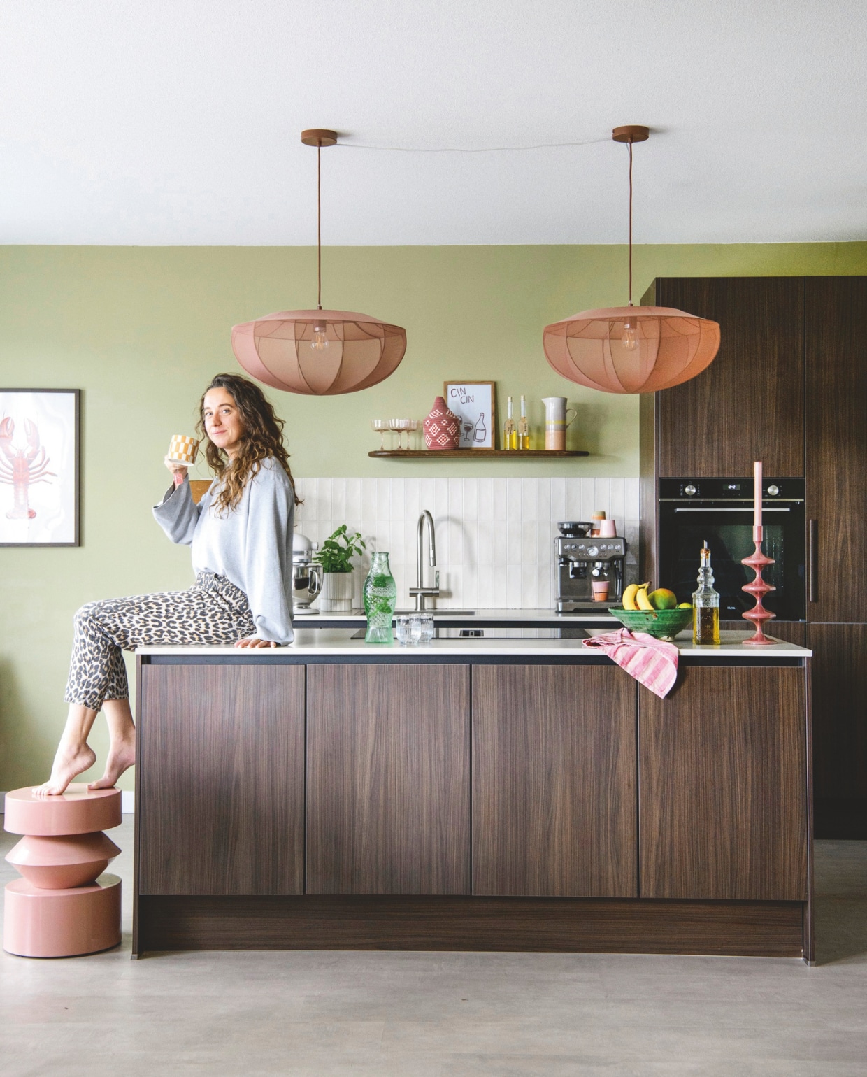 Muurverf Puur Helmgras van Flexa. Keuken Keukenconcurrent. Wandtegels Tegels in huis. Hanglampen Westwing. Wandplank By-Boo. Glazen, theedoek, fruitschaal, kandelaar en lamp met houten voet Loods5. Roze mand Studio Bohome. Karaf HKliving. Schilderij op wandplank zelfgemaakt. Olieflessen kringloop. Glazen fles vis Serax. vtwonen 06-2026 | styling Maaike van Haaster | fotografie Louis Lemaire