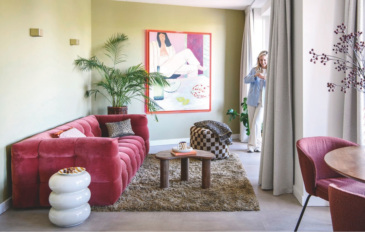 Vloer Karwei. Muurverf Puur Helmgras van Flexa. Bank Sofacompany. Poef, vloerkleed en koffiekop Loods5.Salontafel Home67. Bijzettafel en schotel kringloop. Kunstwerk HKliving. Wandlampen Luminize. Grote plant De Groene Brigade. Sierkussens Enkel Art Studio x Loods5 en HKliving.