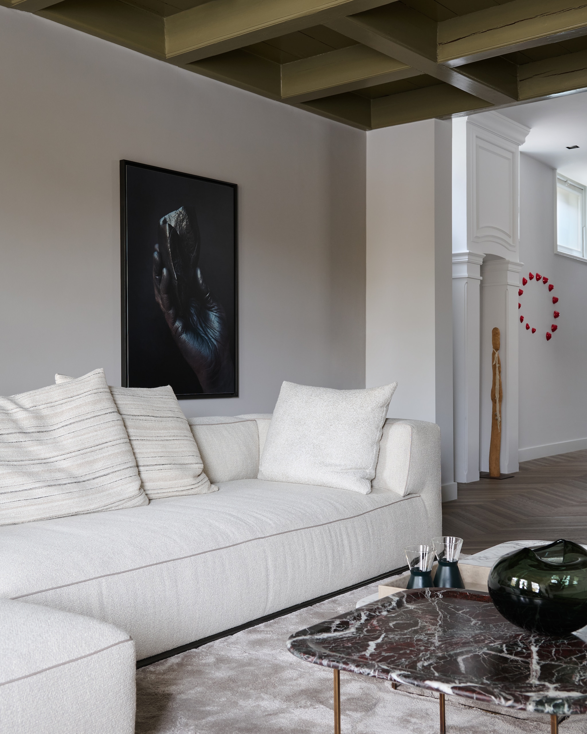Vloerkleed Ozzy van Indivipro, ontwerp Remy Meijers. Bank Flexform.Bijzettafels maatwerk door LenarduzziNatuursteen. Vaas Whenobjectswork. Olielampen IIttala. Kunstwerk René Gonkel. Houten sculptuur Carolina Veerkamp. Rood kunstwerk Simone van Bakel. Houten vloer Barc Flooring. vtwonen design 7-2026 | fotografie Kasia Gatkowska