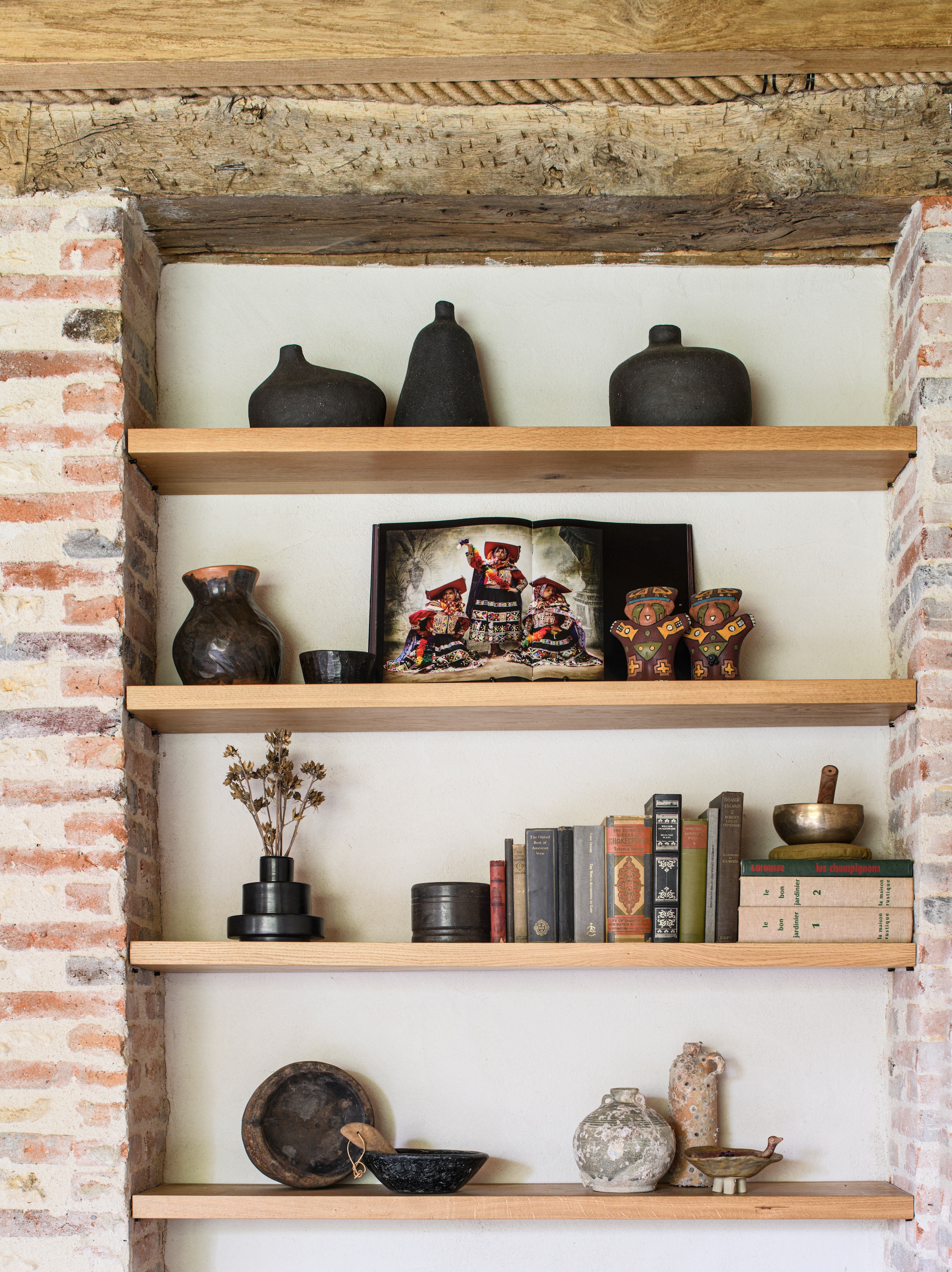 Bovenste plank: potten gemaakt door François’ moeder. Plank eronder: boek Alta Moda van Mario Testino, aardewerk uit Peru. Volgende plank: vaas David Pompa en oude boeken. Onderste plank: schatten 
van Atmosphère D’Ailleurs. vtwonen Landelijk 09-2026 | styling Inge van Lieshout | fotografie Louis Lemaire | productie Insidehomepage