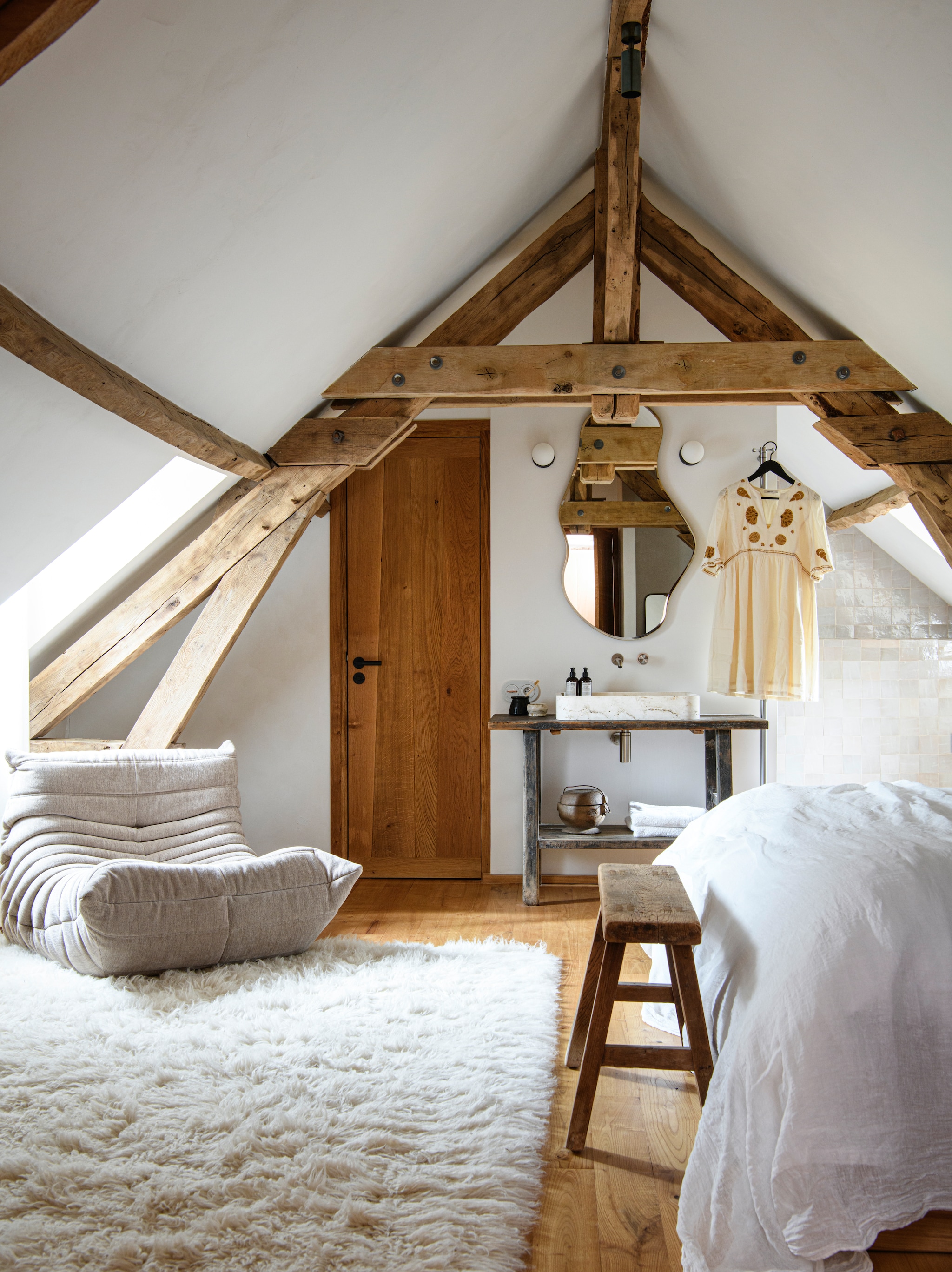 Fauteuil Togo van Ligne Roset. Vloerkleed Cinna. Bed naar  eigen ontwerp op maat gemaakt 
door timmerman. Beddengoed Couleur Chanvre. Spiegel Pond van Ferm Living. Houten bank en 
wastafel Atmosphère D’Ailleurs. Natuurstenen wasbak Vaselli. Lampen David Pompa. Muur 
met natuurlijke kalkverf in kleur Arum van Ressource. vtwonen Landelijk 09-2026 | styling Inge van Lieshout | fotografie Louis Lemaire | productie Insidehomepage
