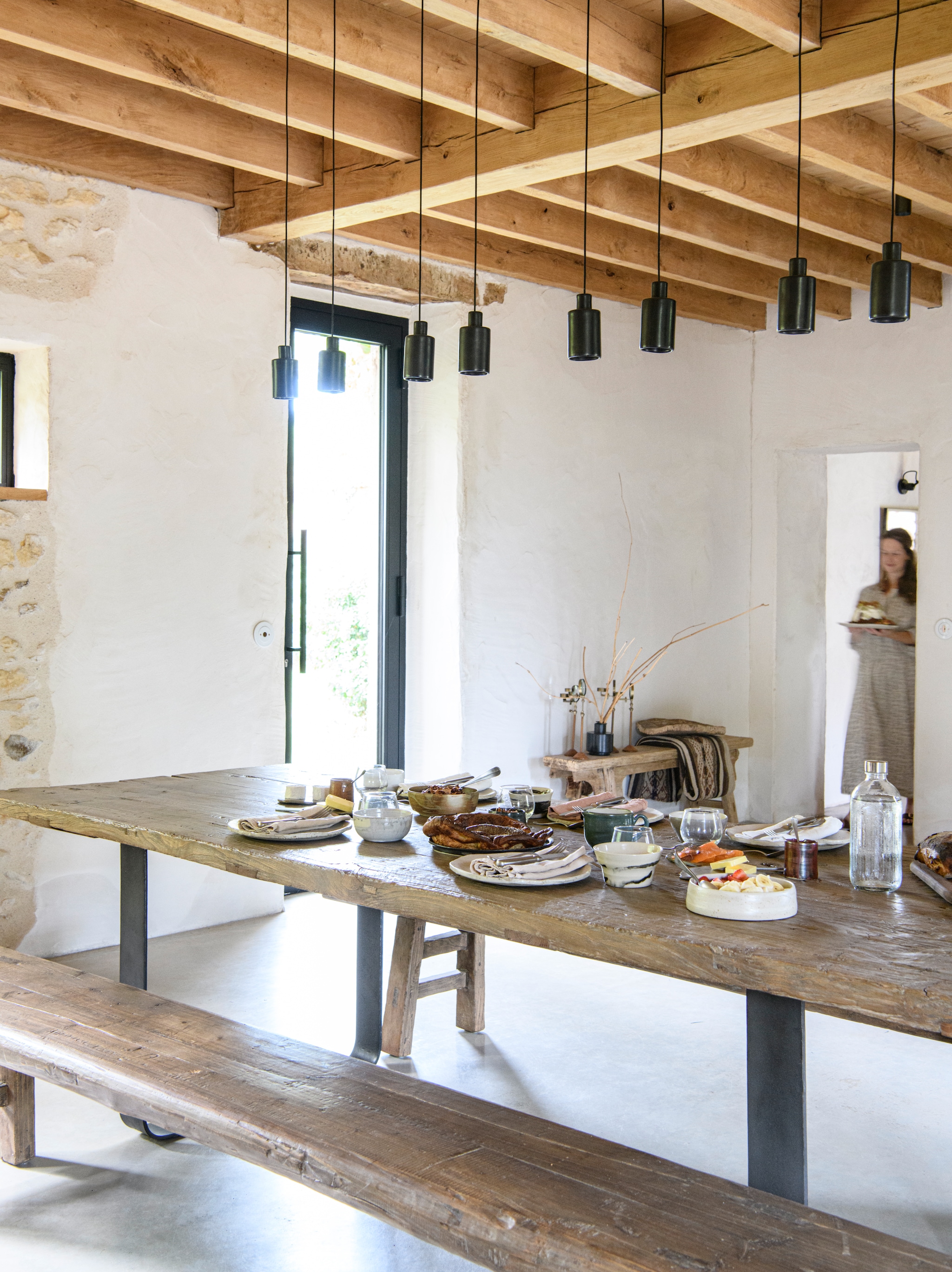 Eettafel en eetbanken Atmosphère D’Ailleurs. 
Hanglampen David Pompa. Wand afgewerkt 
met natuurlijke kalkpleister. Vloer kwartsbeton. vtwonen Landelijk 09-2026 | styling Inge van Lieshout | fotografie Louis Lemaire | productie Insidehomepage