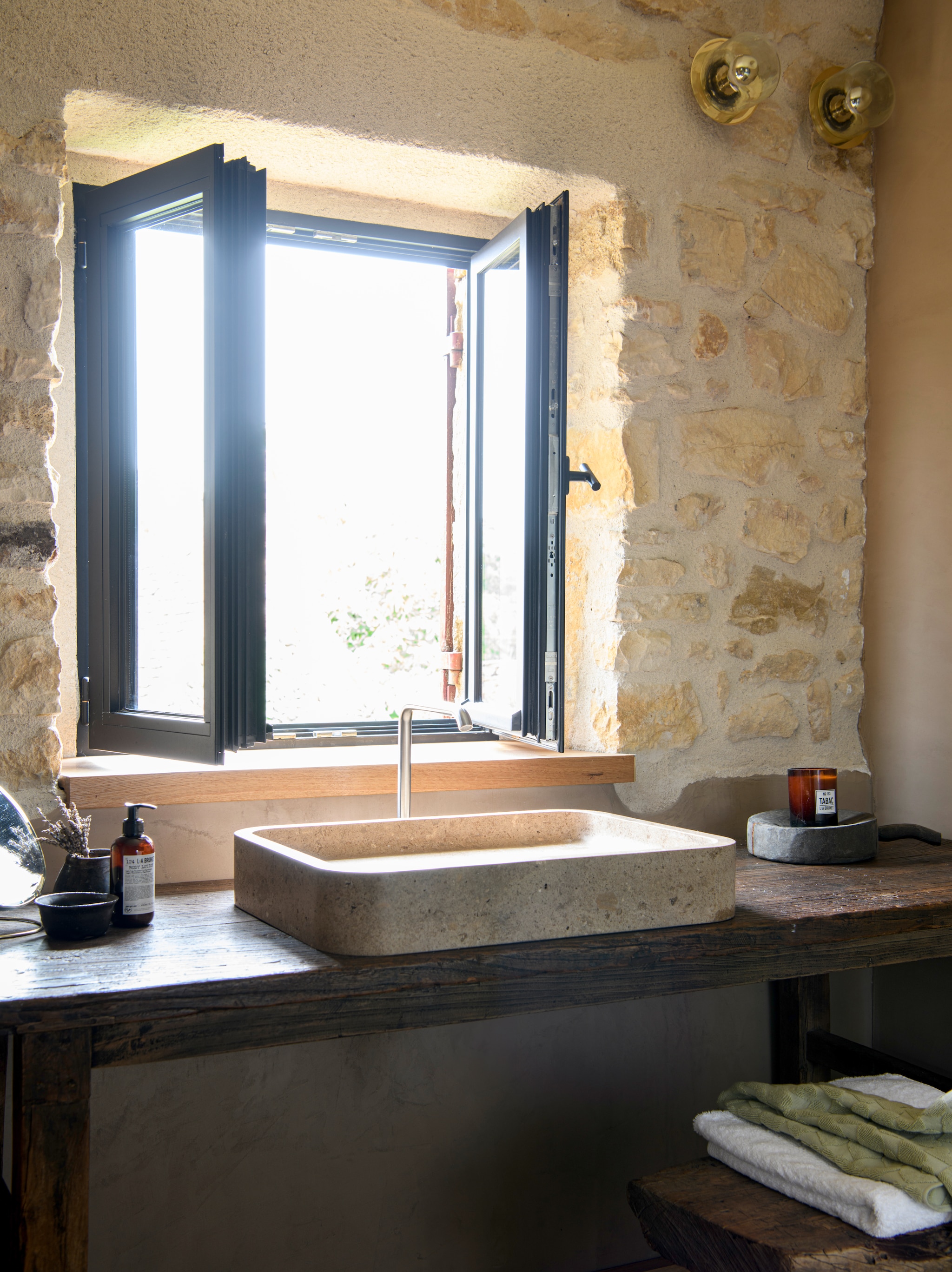 Wastafel Atmosphère D’Ailleurs. Natuurstenen wasbak Vaselli. Wandlampen van gehamerd  
glas en messing David Pompa.  Toiletspullen L:a Bruket. vtwonen Landelijk 09-2026 | styling Inge van Lieshout | fotografie Louis Lemaire | productie Insidehomepage