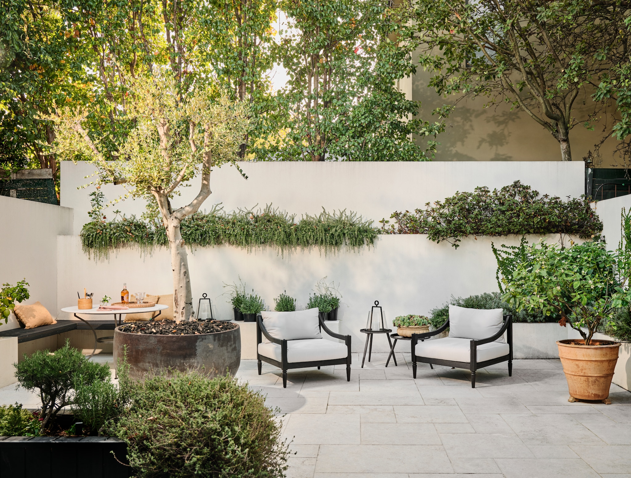 Tafel met marmeren blad Le Forge. Tuinstoelen Coco Republic. Tuinkussens Classic With A Twist. Buitenlantaarns Easton van Pottery Barn. Marmeren buitentegels. vtwonen Landelijk 9-2026 | fotografie Lisa Cohen