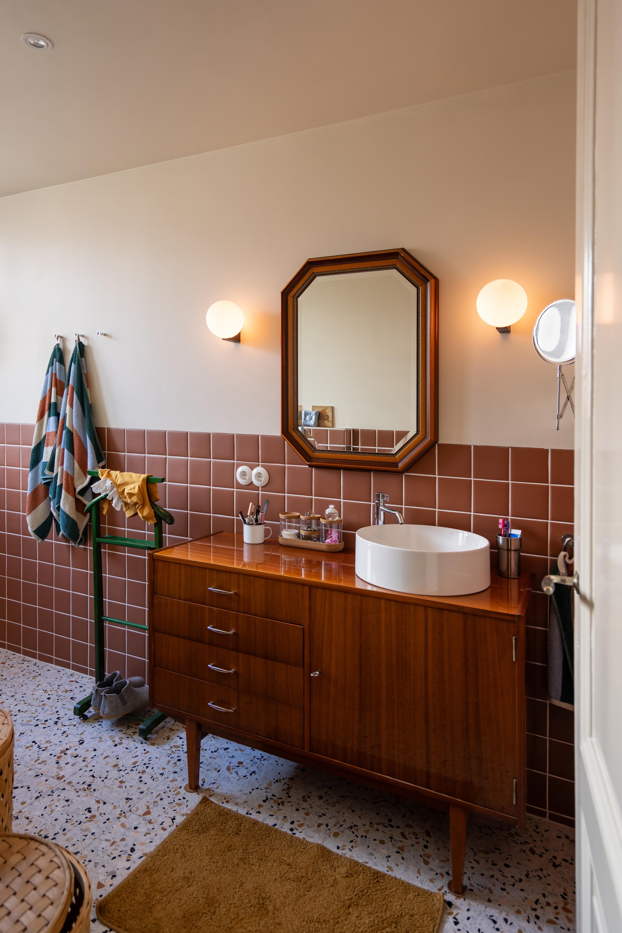 Vintage badkamermeubel Snip Vintage Amsterdam. Tegels Pixel41 kleur tobacco van Tegelfabriek Nederland. Terrazzotegels kleur Firenze 14 van Terrazzo in Huis. Kraan Ivy Kranen. Spiegel kringloop. Wasmand Kwantum. Muurlampen Nostalux. Handdoeken en badmat Hema. Vergrootspiegel Ikea. Handdoekenrek kringloop. vtwonen 09-2026 | fotografie Lotte van Uittert