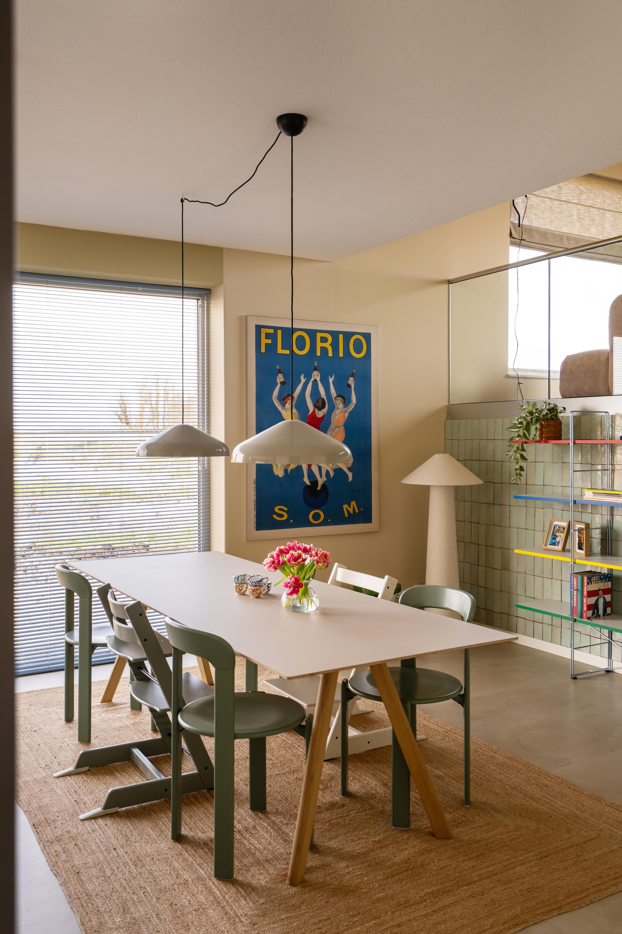 Tafel, stoelen en hanglampen Hay. Kinderstoelen Tripp Trapp van Stokke. Vloerkleed Zara Home. Kunstwerk Florio van Leonetto Cappiello via Werk aan de Muur. Staande lamp Kwantum. Tegels Platta Vert Clair via Designtegels. Aluminium jaloezieën Allure in Baby Blue van Veneta. Boekenkast Ikea. Muurkleur Wild Wonder van Flexa en Joa’s White van Farrow & Ball. Vloer Stanmore dryback beige van Floorlife. vtwonen 09-2026 | fotografie Lotte van Uittert