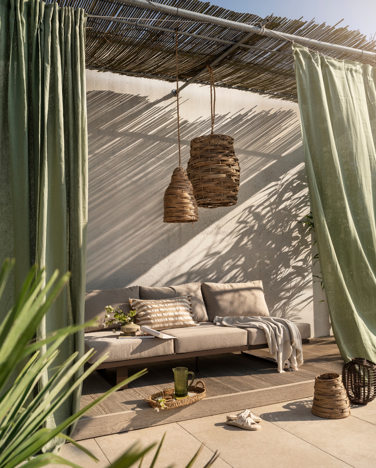 Woood tuinbank Bear 3-zits, outdoor stof en aluminium, bruin, 210x87x80 cm (bxdxh) € 999,- (shop.vtwonen.nl). Gommaire hanglamp Irving Xl, rotan, naturel € 295,-, hanglamp Nest, rotan, naturel € 199,-, mand Nest groot, wicker en pitriet, naturel € 60,- (gommaire.com). Ikea gordijnen Dytåg, katoen en linnen, grijsgroen, 300x145 cm (lxb), set van 2 € 69,99 (ikea.nl). Zara Home gestreepte kussenhoes, katoenmix, beige, 60x40 cm (lxb) € 39,99, deken met franje, katoenmix, ecru, 180x240 cm (lxb) € 39,99, glazen kan, reliëfmotief, glas, groen € 25,99 (zarahome.com). H&m Home kleine vaas, keramiek, beige € 14,99, ovaal dienblad, zeegras, naturel € 24,99, espadrilles met gedraaid detail, beige € 14,99 (hm.com). Kwantum lantaarn Bradford, bamboe, bruin € 19,99 (kwantum.nl). Overig privébezit.