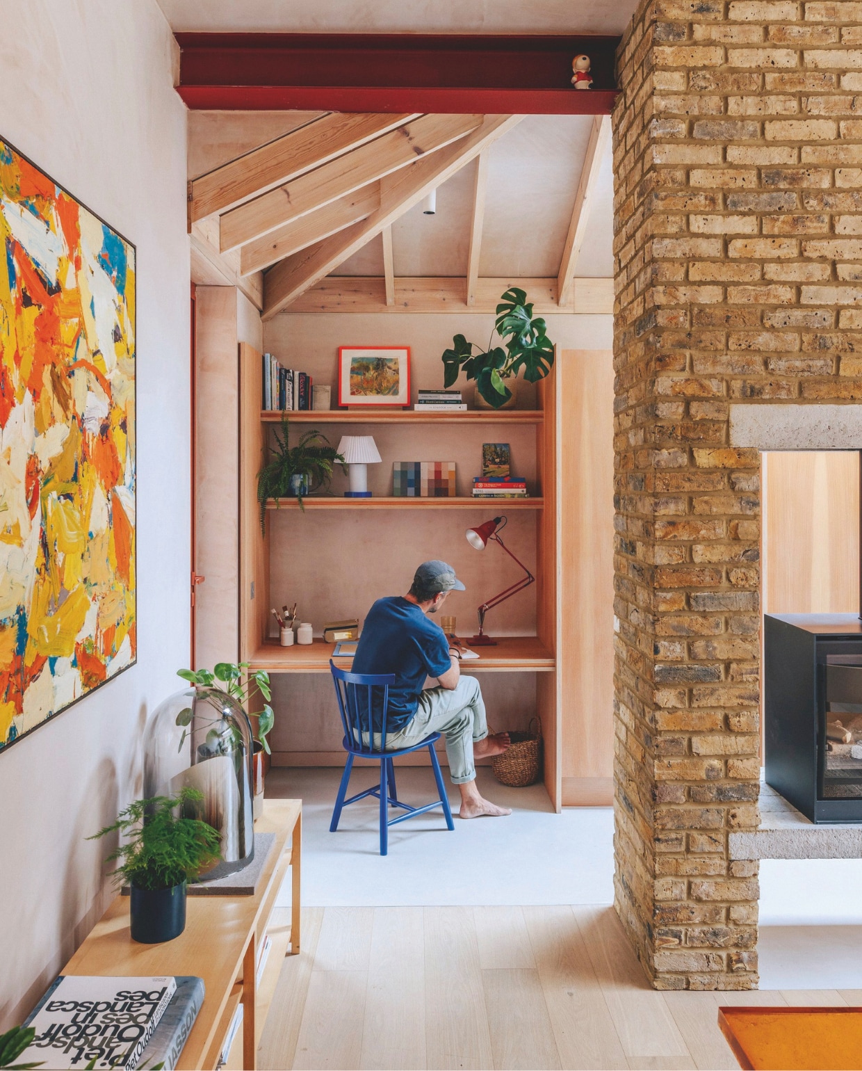 Stoel J46 van Fdb Møbler. Maatwerk werkhoek afgewerkt met Douglas-fineer. Tafellamp Cellu van Normann Copenhagen. Bureaulamp Original 127 van Anglepoise. Pennenzak Penco Carry Tite van High-tide. Kunstwerk in rode lijst: Plastic Cactus van Jack McGarrity. Op de onderste plank schilderij Harry Parker. Schilderij links Thea’s van Tom Robinson via Messums Gallery. Dressoir en stolp Rolf Sachs. Tafellamp in stolp Ikea.