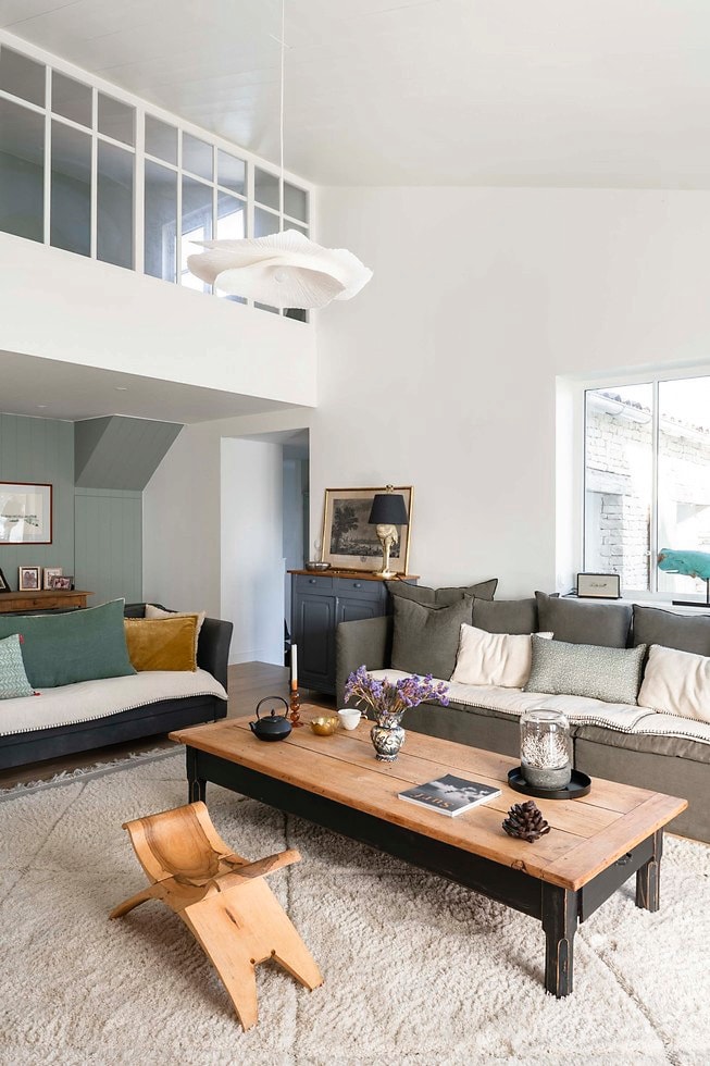 Bank Maison de Vacances. Fauteuils uit de familie. Saramaka-krukken uit Frans-Guyana meegebracht. Salontafel en dressoir Brocante Marchand d’Oublis. Kussens La Redoute. Hanglamp Zara Home. Vloerkleed berber uit Marokko. Tafellamp Kare Design. Walvissculptuur lokale boetiek Migration. Gordijnen Mondial Tissus. vtwonen Landelijk 6-2026 | styling Amandine Berthon | fotografie Julien Fernandez