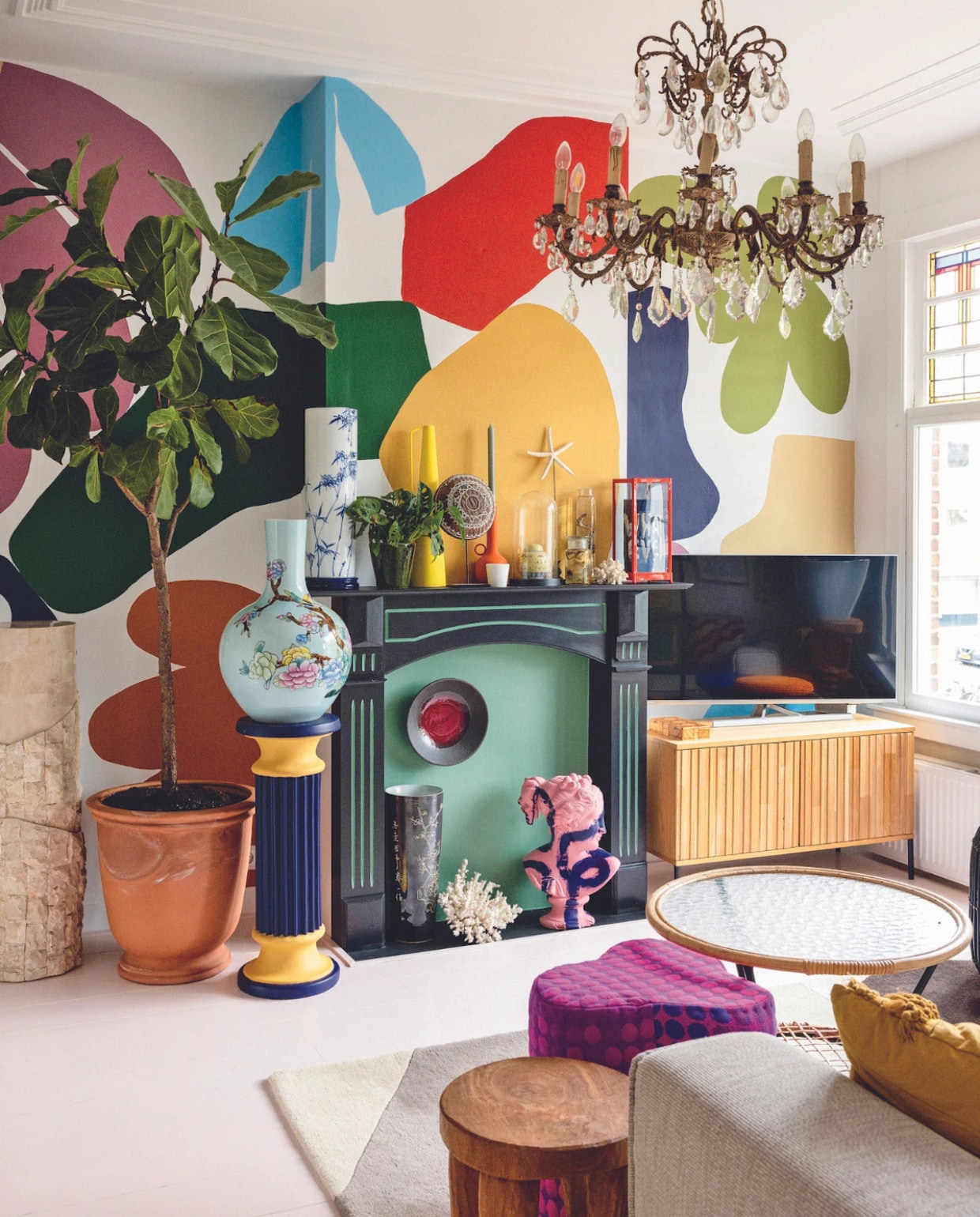 Marmeren zuil en zelf geschilderde pilaar Marktplaats. Terracottapot tuincentrum. Gebloemde vaas, gele vaas, oranje kandelaar, poef en houten bijzettafel Polspotten. Lamp vintage. Vitrinekast, donkere vaas, koraal en bijzettafel met glazen blad kringloopwinkel. Blauwe vaas gemaakt door Sharvin, tv-meubel Woood, bord Norman Trapman, plant Marvy Green. Overig onbekend.