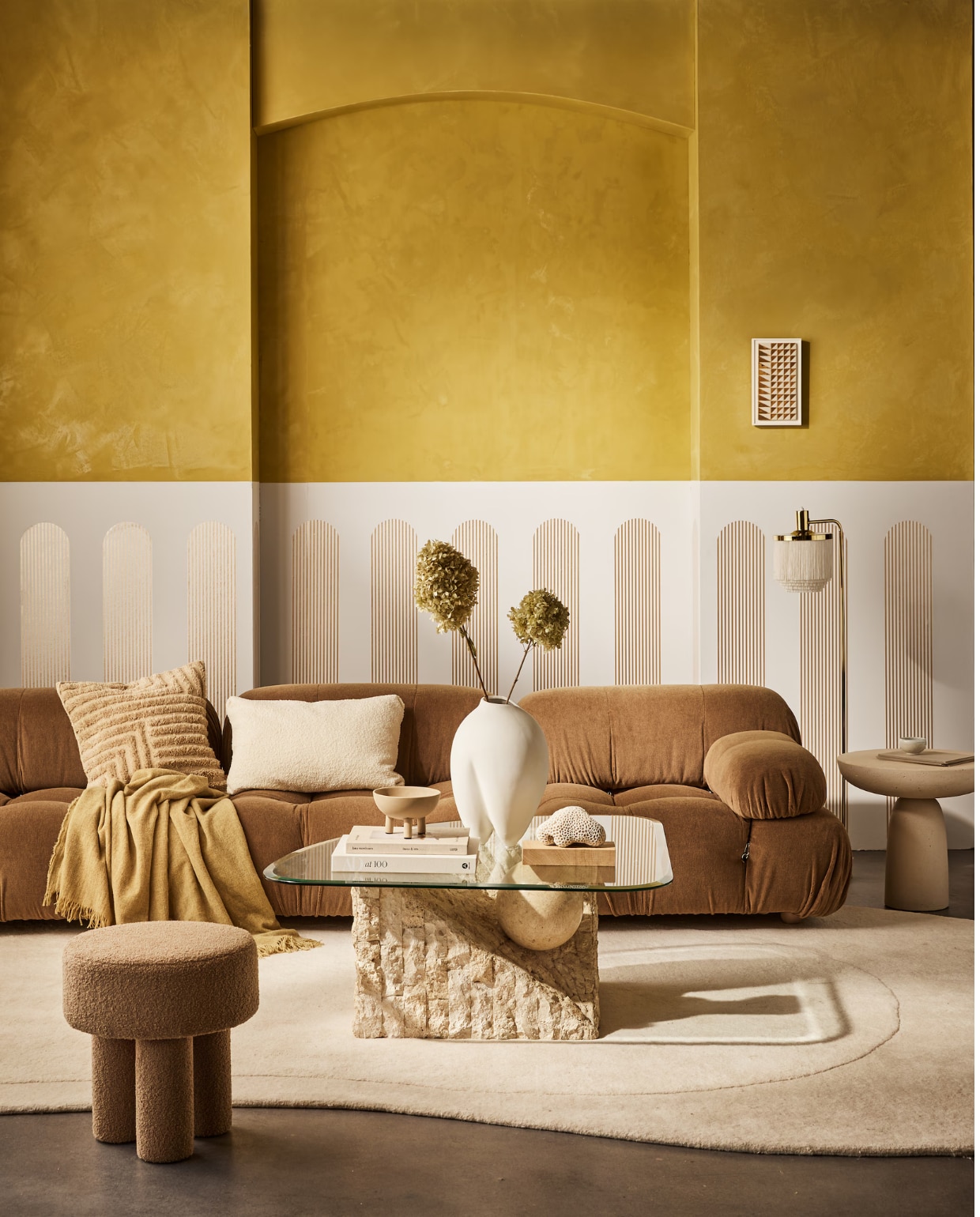 vtwonen collectie behangstrook Streep Gold-Egg White, 17,6 cm (b), rol van 10 m. M.m.v. homestede.nl (bank, kussens, plaid), edha-interieur.nl (poef, bijzettafel), goeds.nl (vloerkleed van Layered, lamp), pietjonker.nl (salontafel), rollmannceramics.com (kunsttegel), lauthentique.nl (gele muurverf kalkverf in Korengoud 33, witte muurverf krijtverf in Krijt 63), 101cph.com (vaas, schaal). Overig privébezit. vtwonen collectie 02-2023 | productie Tanja Saarberg | styling Cleo Scheulderman | fotografie Jeroen van der Spek | assistentie Kelly van Gendt | studio en decorbouw Studio Milo