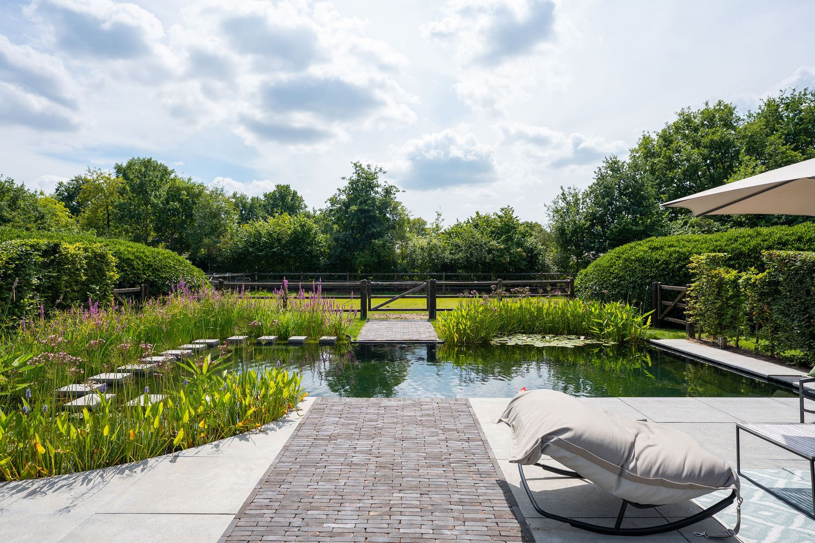 Natuurlijke zwemvijver met zwemzone van 5x10 m, waterlelies en oeverbeplanting door LilyPond (lilypond.nl). vtwonen Landelijk 08-2026