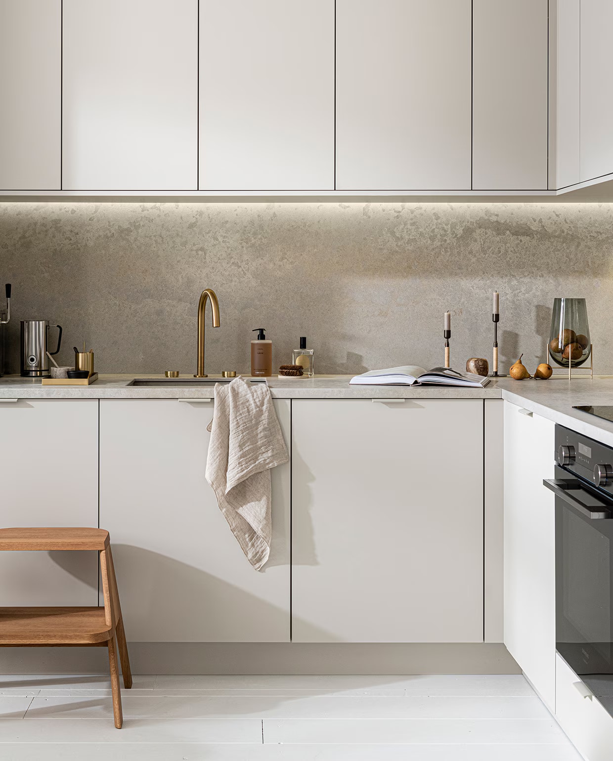 Keuken Basic Greige via Mandemakers. M.m.v. thefinestore.com (houten krukje van Hay, messing dienblad en beker van Ferm Living, bronzed brass kandelaren Duca van Menu), flinders.nl (vaas van gerookt glas op messing pootjes van Menu), kikubari.nl (spray van Lingua Planta), vtwonen.nl (theedoek uit de vtwonen collectie), skins.nl (handzeep Suede Byredo), sjostrandcoffee.nl (melkschuimer). Overig privébezit. vtwonen 03-2021 | productie Tanja Saarberg | styling Kim van Rossenberg | fotografie Sjoerd Eickmans
