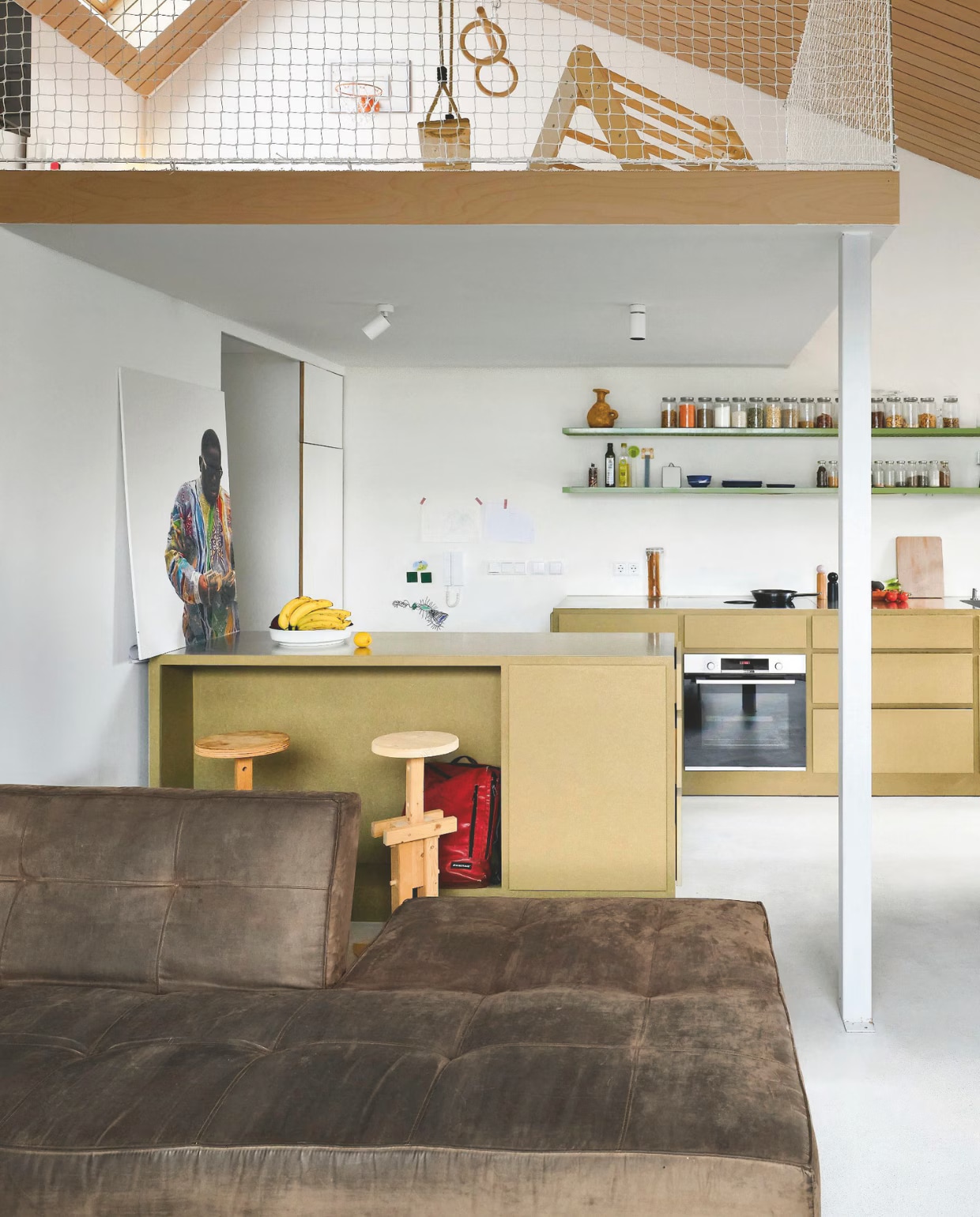Houten krukken en hanglamp eigen ontwerp van Dirk. Keuken van gecoat vochtwerend mdf met wandplanken van gekleurde rasters van rvs. Op de plank: vaas van Willem van Hooff. Houten tafel is een oud bureau van Alissa. Kunstwerk links cadeau van vrienden. Stoelen Brabantia, opnieuw bekleed. Bank Splitback van Innovation Living. vtwonen 06-2026 | fotografie Mr. Frank