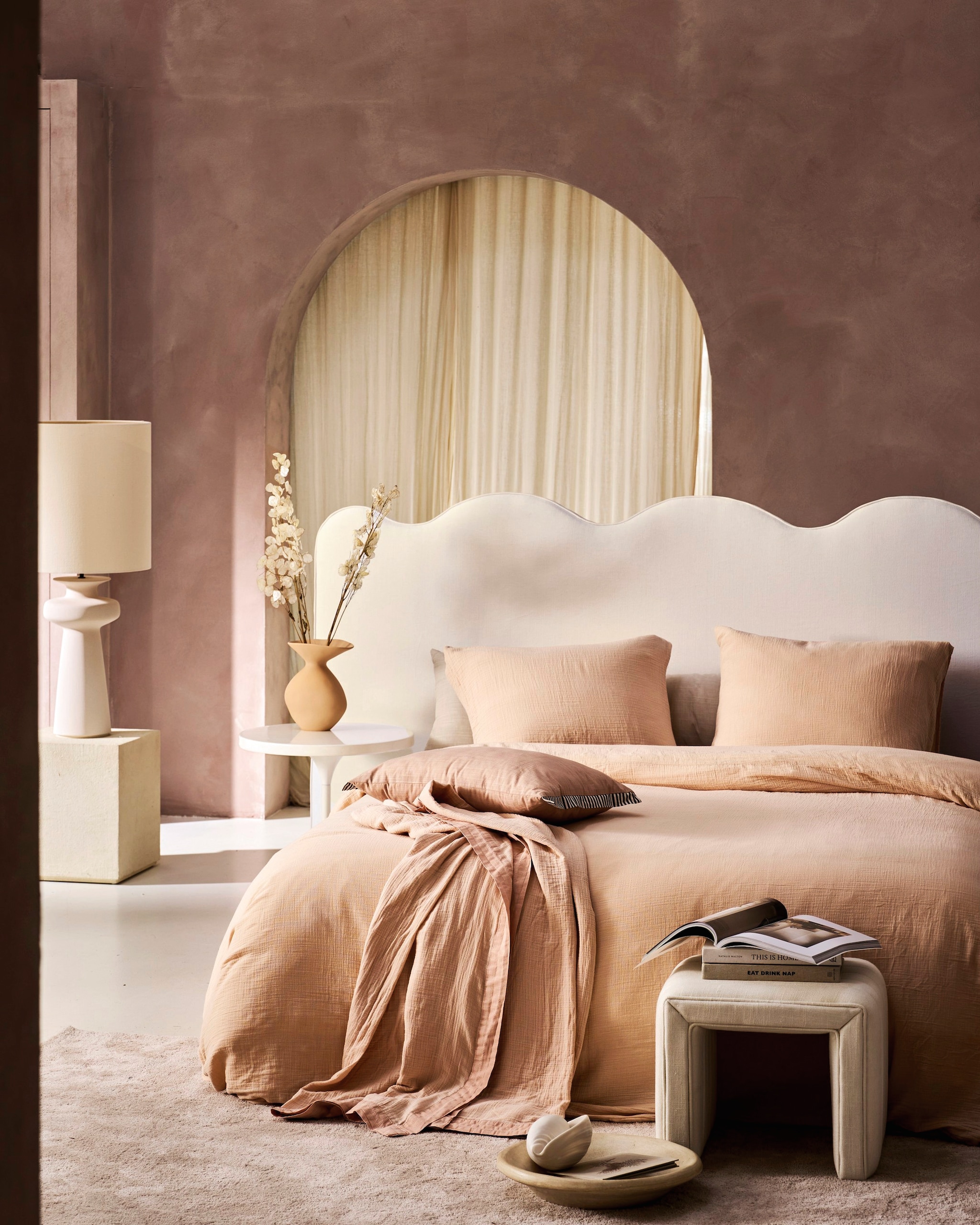 vtwonen dekbedovertrek Gentle Embrace, katoen mousseline, soft pink, vanaf € 59,95, vtwonen sierkussen Cozy Slub, katoen slub en polyester (vulling), 60x40 cm (lxb) € 44,95, vtwonen bedsprei Gentle Embrace, katoen mousseline, soft pink, vanaf € 59,95.M.m.v. urbannatureculture.com (gestoffeerde bank, ronde bijzettafel, vaas), stoffeershop.nl (headboard op maat gemaakt), romo.com (stof Linara Chalk mix voor headboard), deens.nl (schelp van Mette Ditte), versmissen.nl (tafellamp Nash), zarahome.com (kubus, bijzettafel). Overig privébezit. vtwonen collectie 7-2026 | styling Cleo Scheulderman | fotografie Jeroen van der Spek
