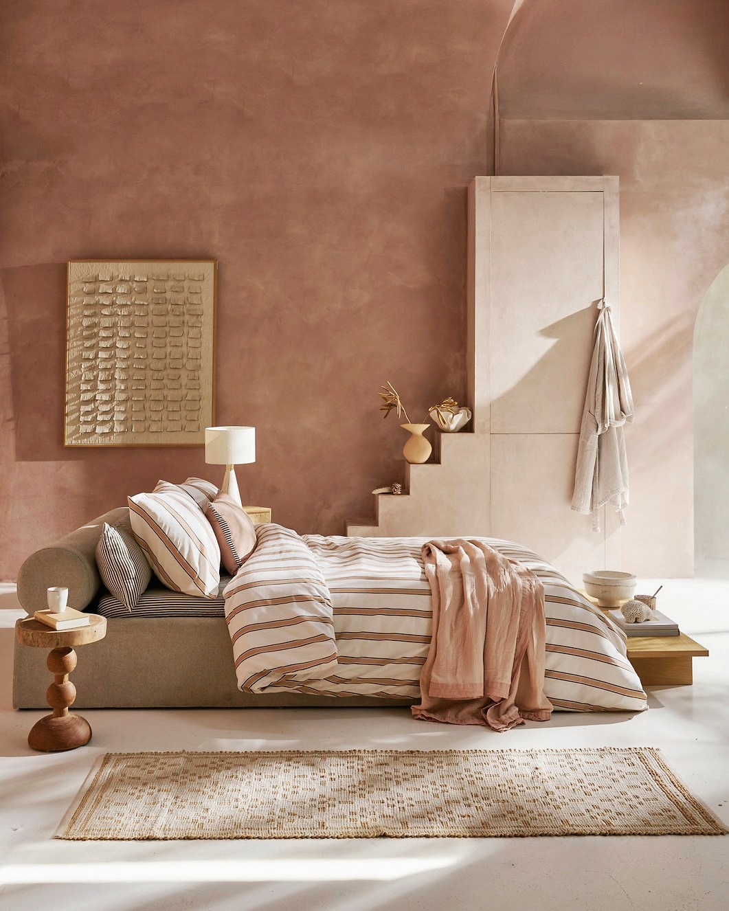 vtwonen dekbedovertrek Fun Stripe, katoen, naturel, vanaf € 59,95, vtwonen bedsprei Gentle Embrace, katoen mousseline, soft pink, vanaf € 59,95, vtwonen hoeslaken Mini Stripe, katoen, naturel, vanaf € 19,95, vtwonen sierkussen Mini Stripe, katoen, naturel, 150x40 (lxb) € 69,95, vtwonen sierkussen Cozy Slub, katoen slub en polyester (vulling), 60x40 cm (lxb) € 44,95. M.m.v. urbannatureculture.com (tafellamp, vaas), deens.nl (schelp van Mette Ditmer, vloerkleed van Madam Stoltz), versmissen.nl (bijzettafel en kunstwerk). Overig privébezit.