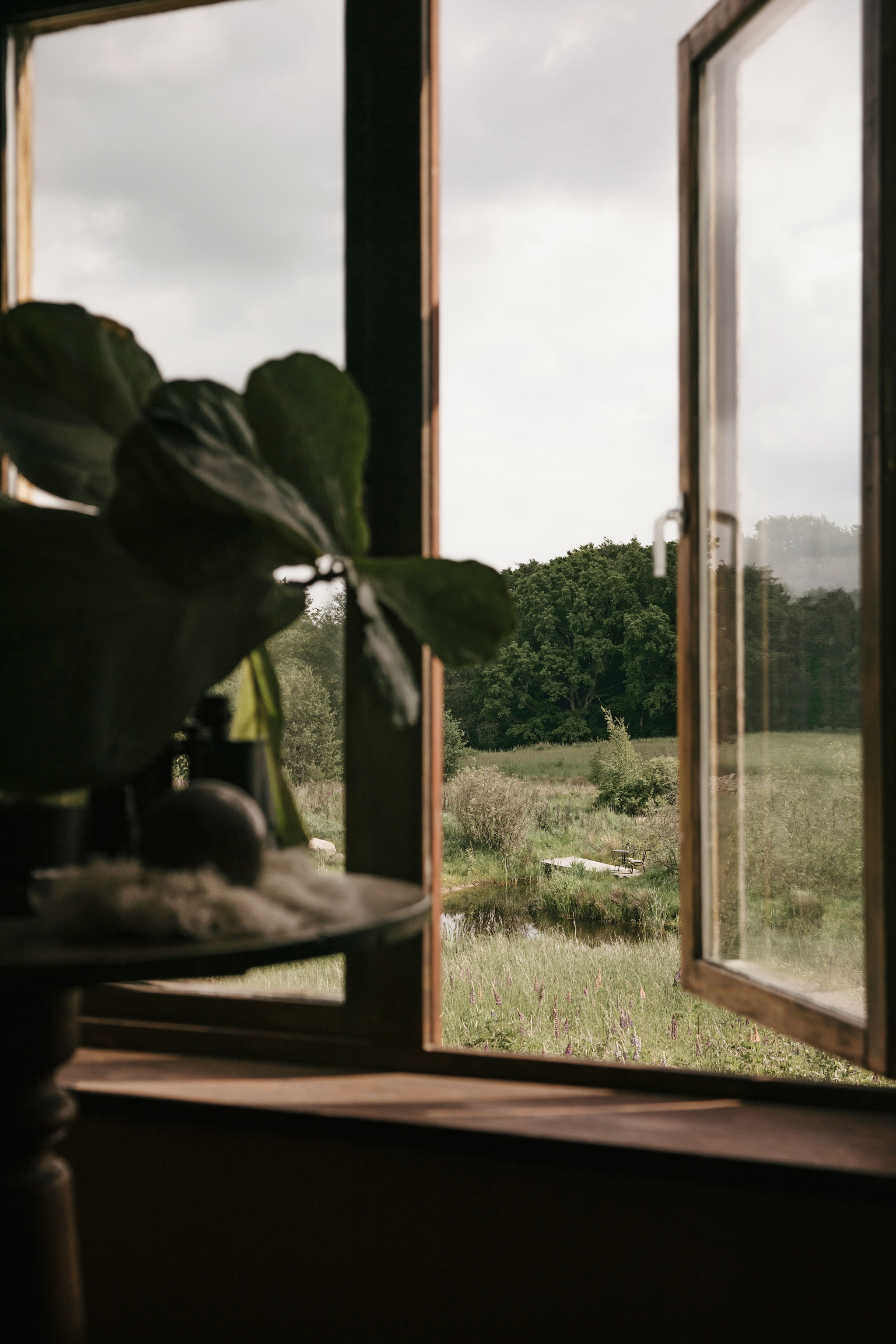 Uitzicht over het meer en de houten brug naar het eiland. vtwonen Landelijk 10-2026 | Styling Karolina Vertus | Fotografie Isabell N Wedin | Productie Living Inside