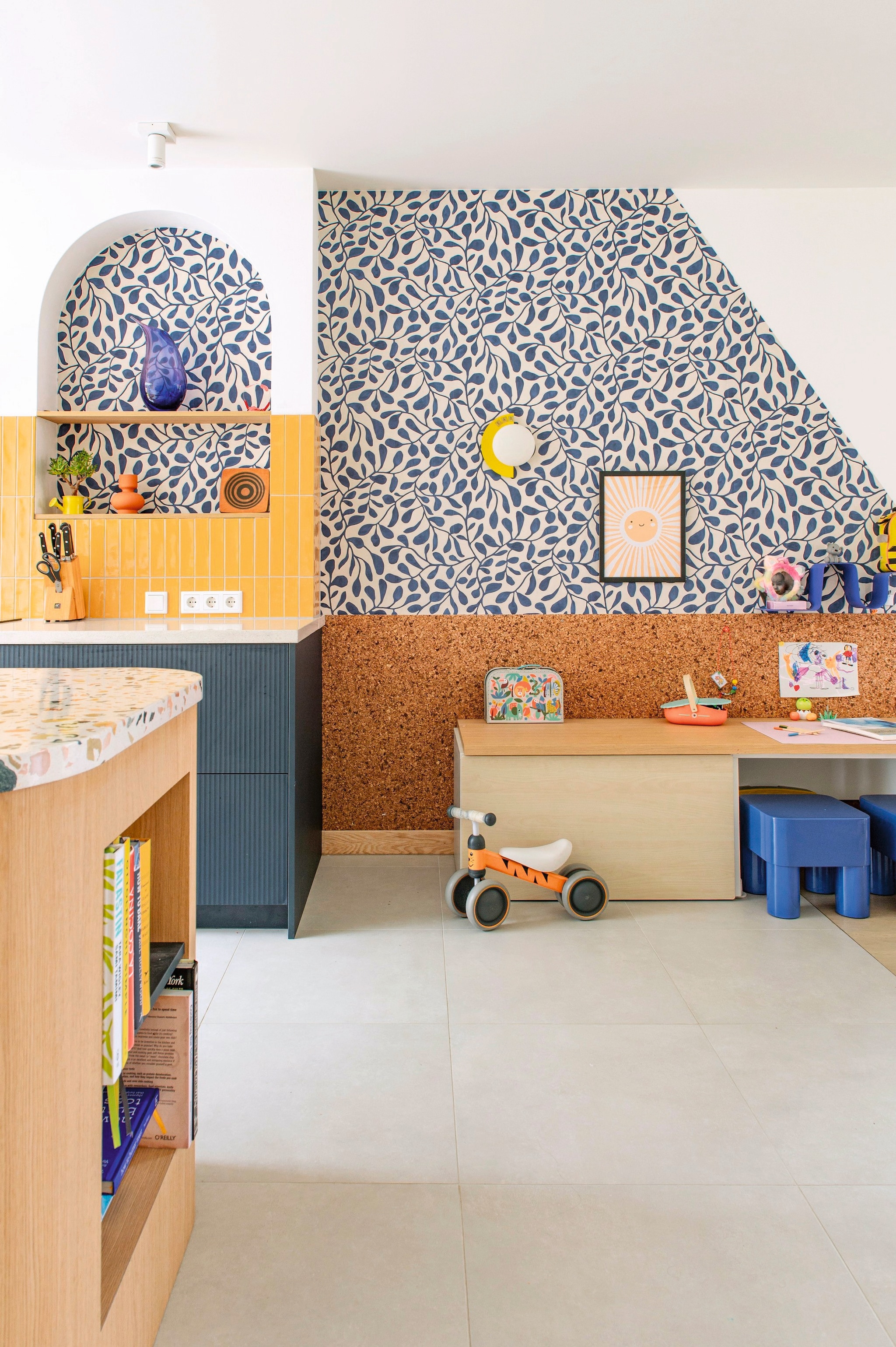 Behang Twist van Eijffinger. Kurkwand Kurk24. Speeltafel Ikea. Krukken Chubb en blauwe wandplank van Jotex. Poster Poster Store. Keuken Jorik Maakt. Tegels Luz Giallo van Marazzi. Muurkleur Wevet van Farrow & Ball.