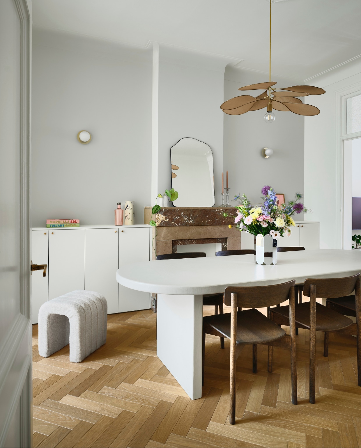 Wandkasten maatwerk naar eigen ontwerp. Messing greepjes op kasten en messing deurklinken Dauby. Poef Kwantum. Tafel maatwerk naar eigen ontwerp, afgewerkt met microtopping van B.a.i.t. Stoelen Takt. Hanglamp Georges via Couleur Locale. Wandlampen H&m Home. Vaas spiegelglas Muller Van Severen voor Hay. Spiegel Zara Home. Kandelaars vintage. Interieurboeken Assouline. Waterfles Paveau. Eiken visgraat parket Avance in Valetta via Hout Luyten. vtwonen 07-2026 | fotografie Mr. Frank