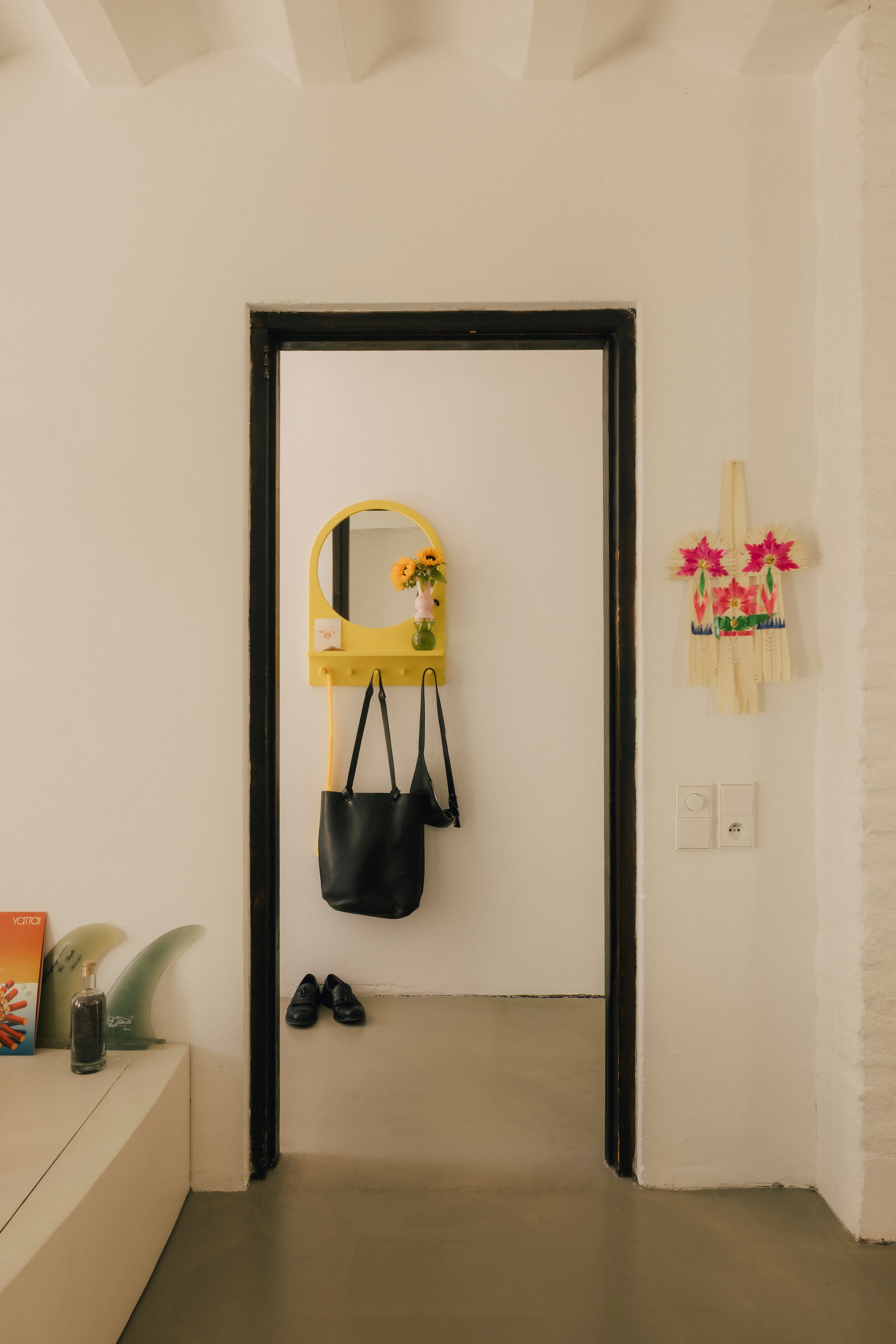 Spiegel met haken, vintage Ikea. Originele kozijnen uit het landhuis waar dit huis deel van uitmaakte, gebrand en in de was gezet. Balinees ceremonieel wandkunstwerk souvenir. Surfboard Fin Volan 4A van True Ames. vtwonen design 8-2026 | Fotografie Katoo Peeters