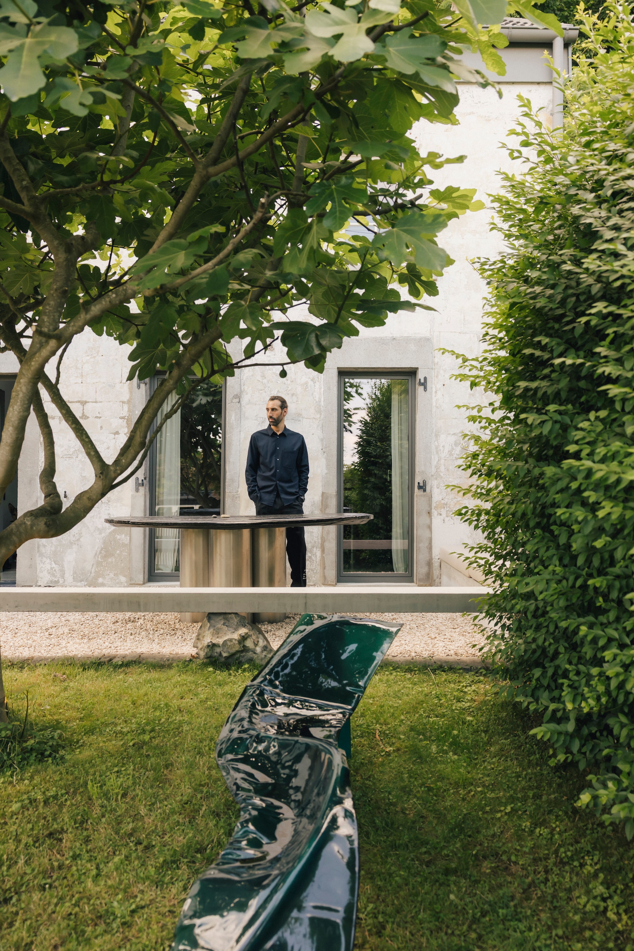 Buitentafel met rvs onderstel en oud wijnvatdeksel van verkoold eikenhout. Betonnen bank met natuurlijke Silexsteen uit de berg achter het huis als steunpilaar.Beide van Lukas Cober. vtwonen design 8-2026 | Fotografie Katoo Peeters